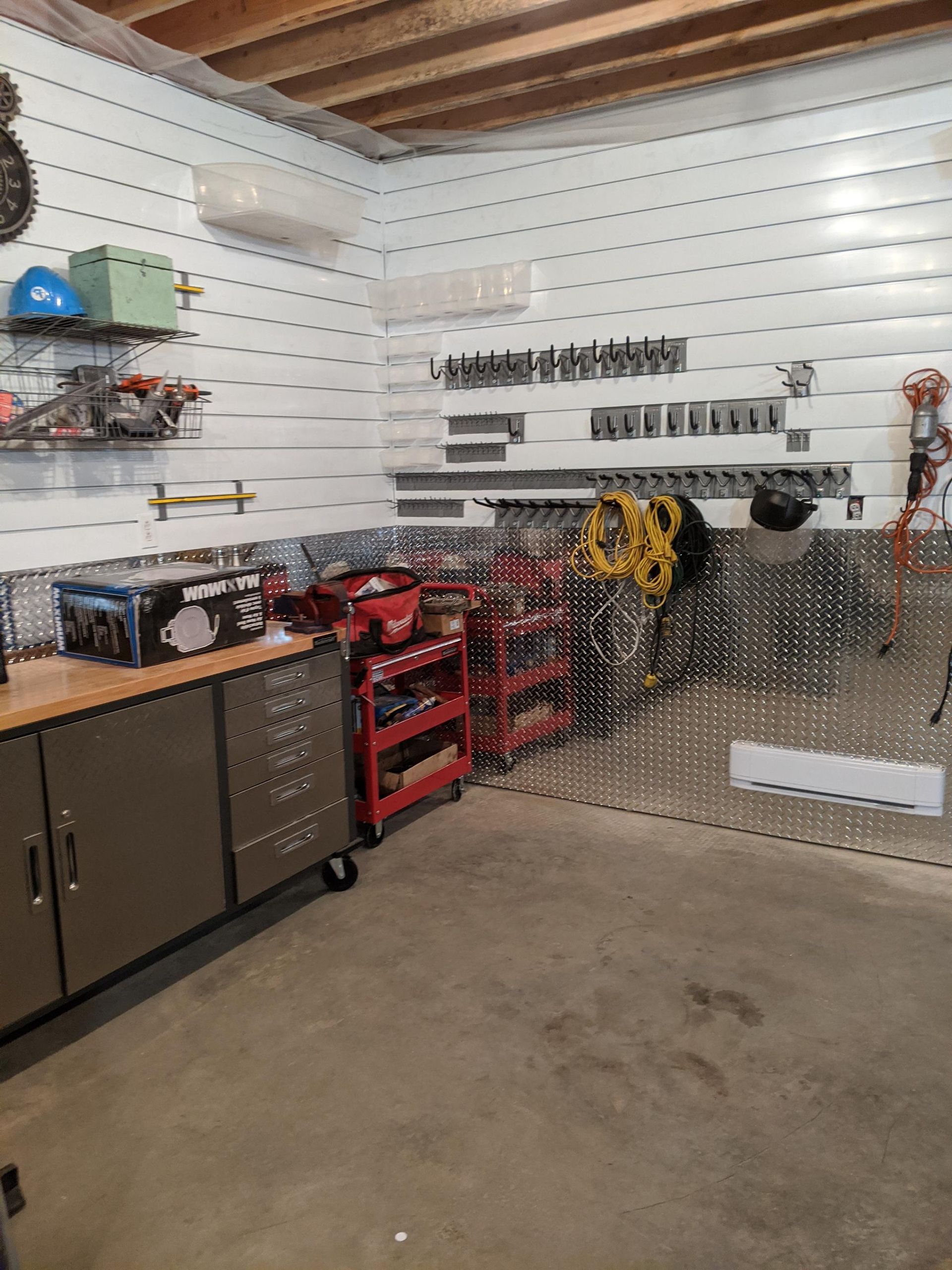 Intérieur de garage avec outils, armoires et plans de travail. Murs blancs avec objets fixés au mur. Sol en béton.