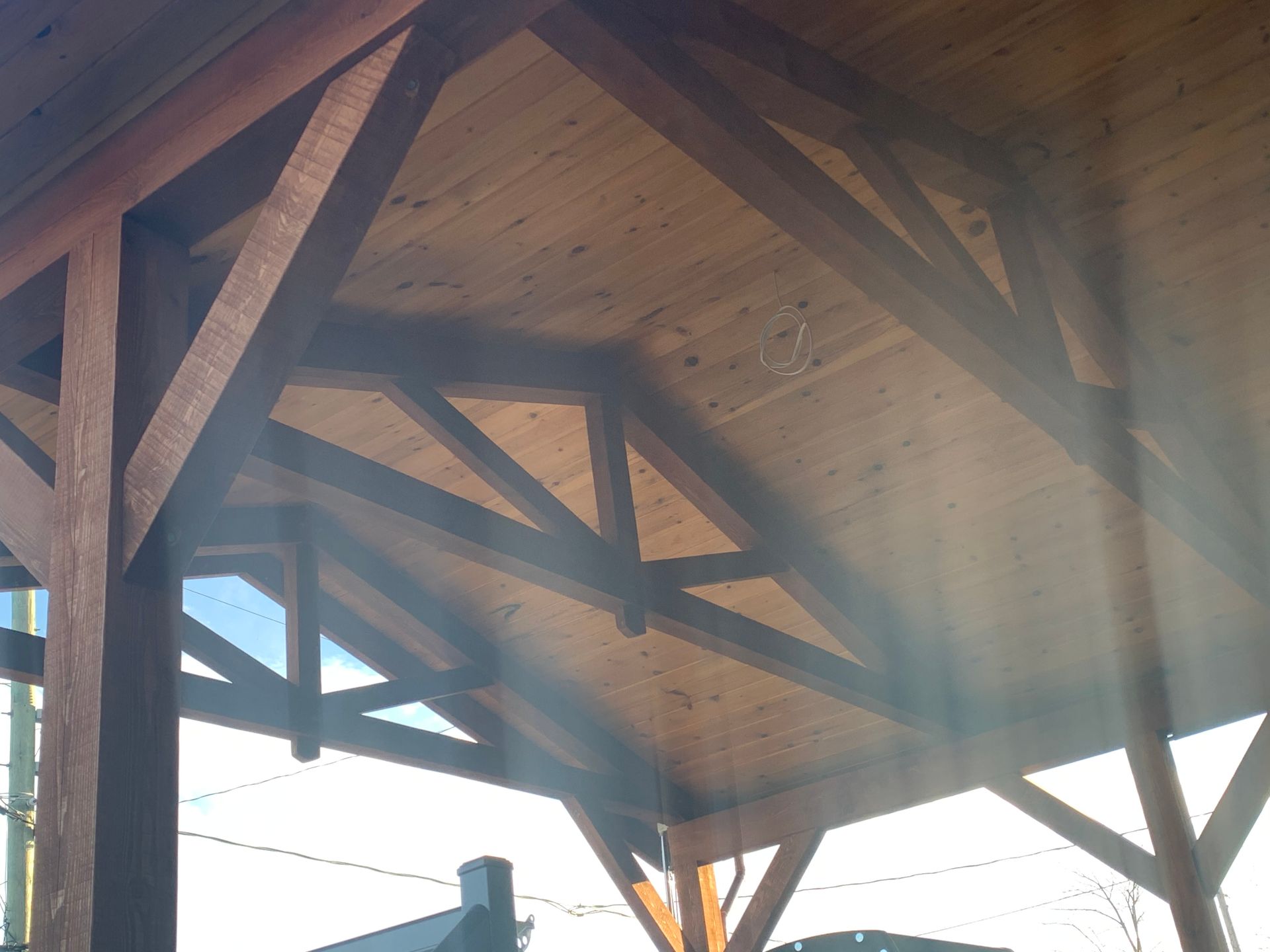 Plafond en bois avec poutres et chevrons, teinté brun, vu d'en bas sous une lumière vive.
