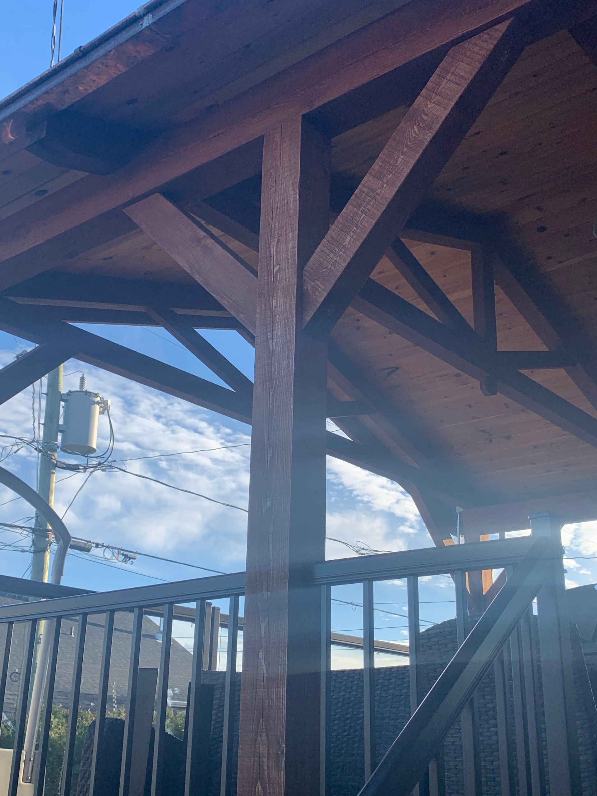 Pergola en bois avec poutres brunes, ciel bleu et balustrade.