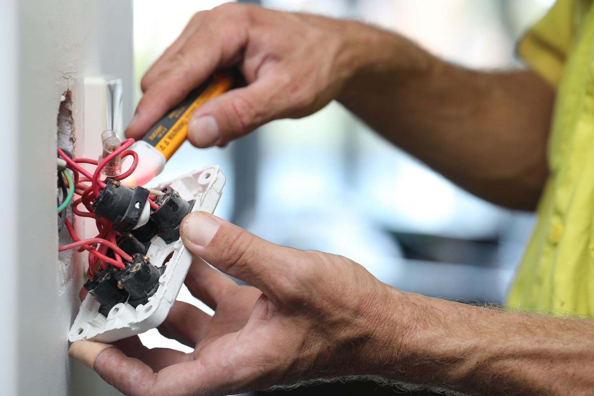 Electrician using a voltage tester on wires in a wall.