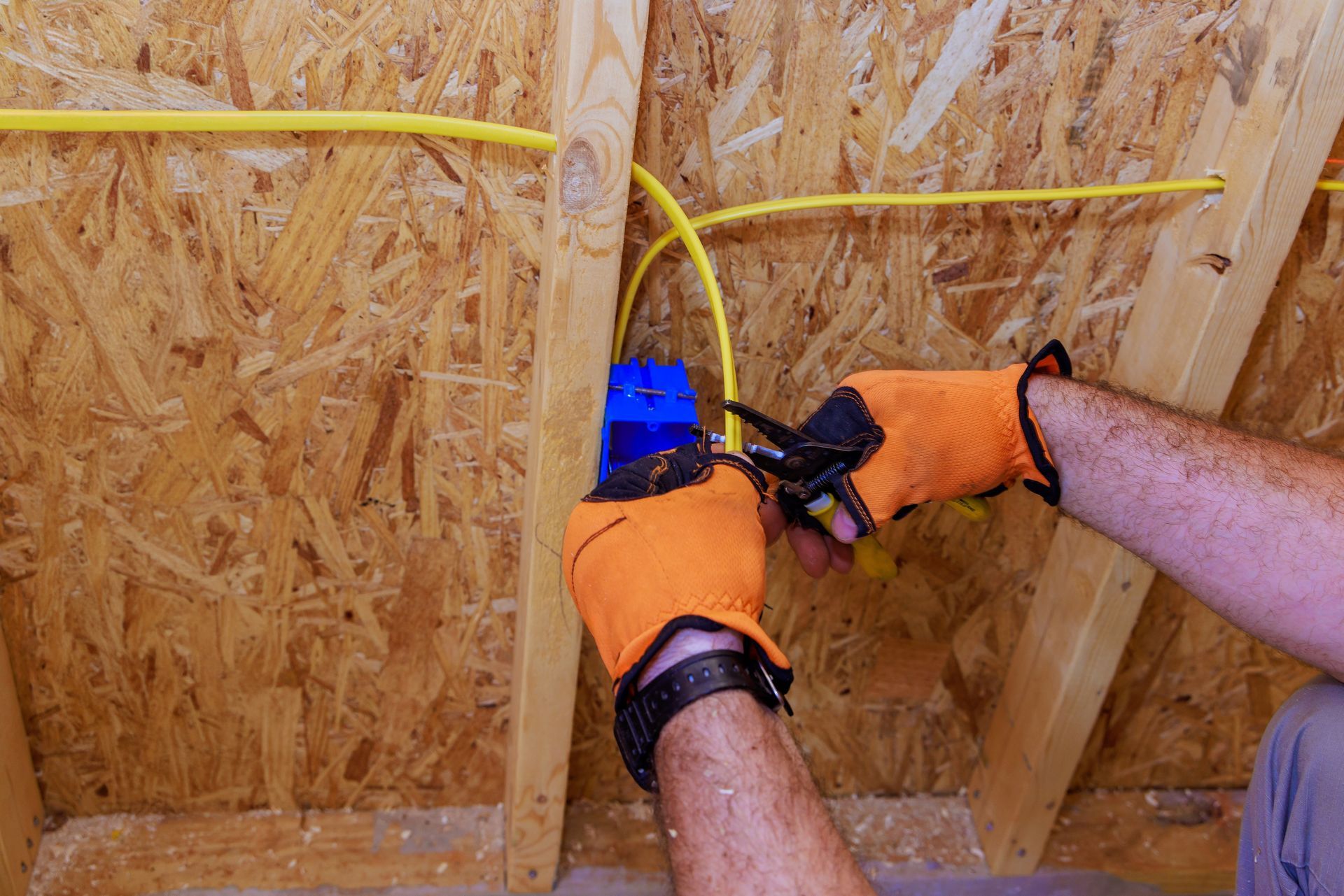 Person in orange gloves wiring electrical box in attic with yellow cables.