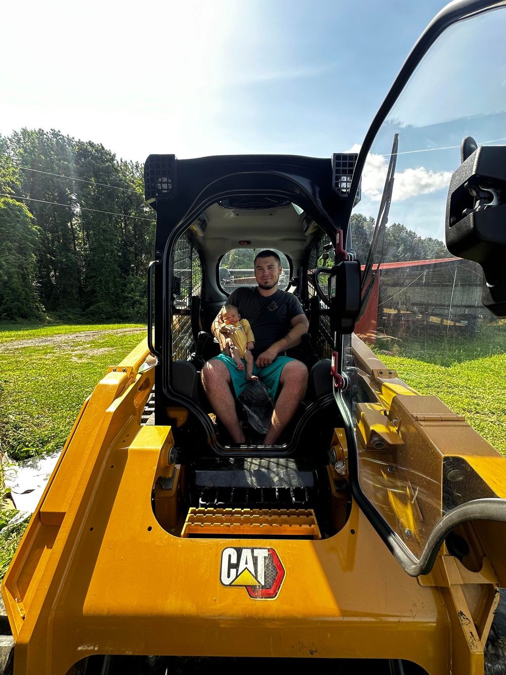 Two people seated in a yellow CAT machine, viewed from the cab on a sunny outdoor site