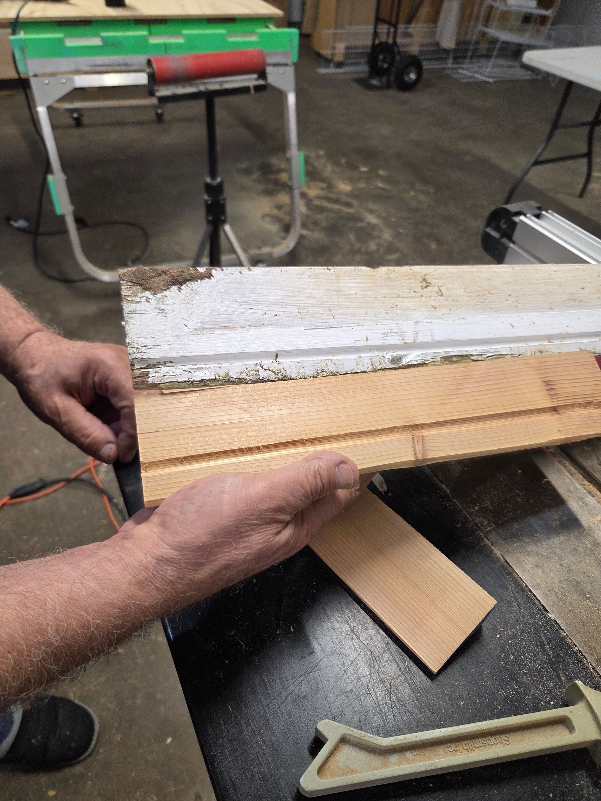Hands holding a layered wood or composite board in a workshop, with a white textured strip on top.