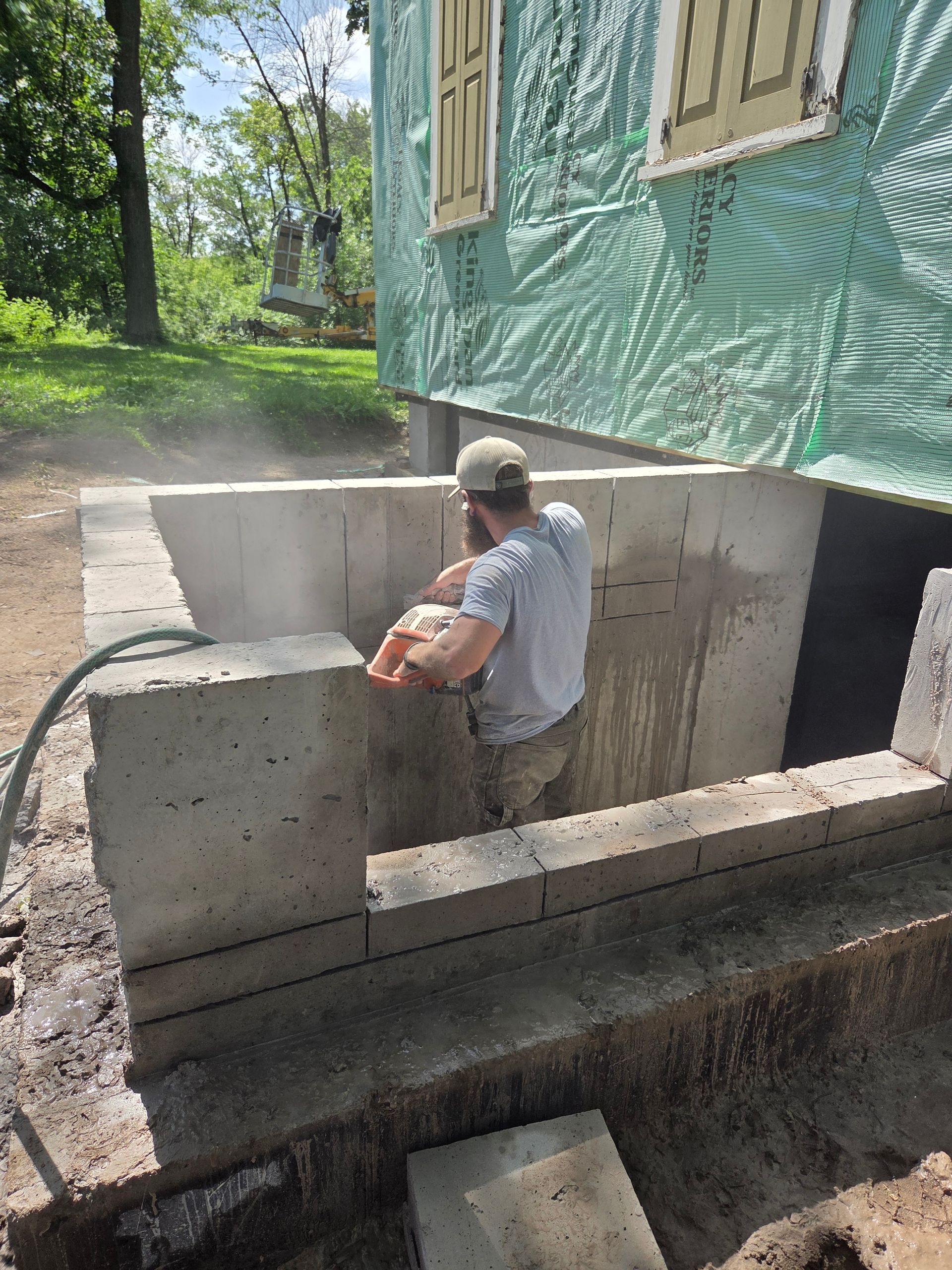 Worker in a hard hat installing concrete forms beside a green house.