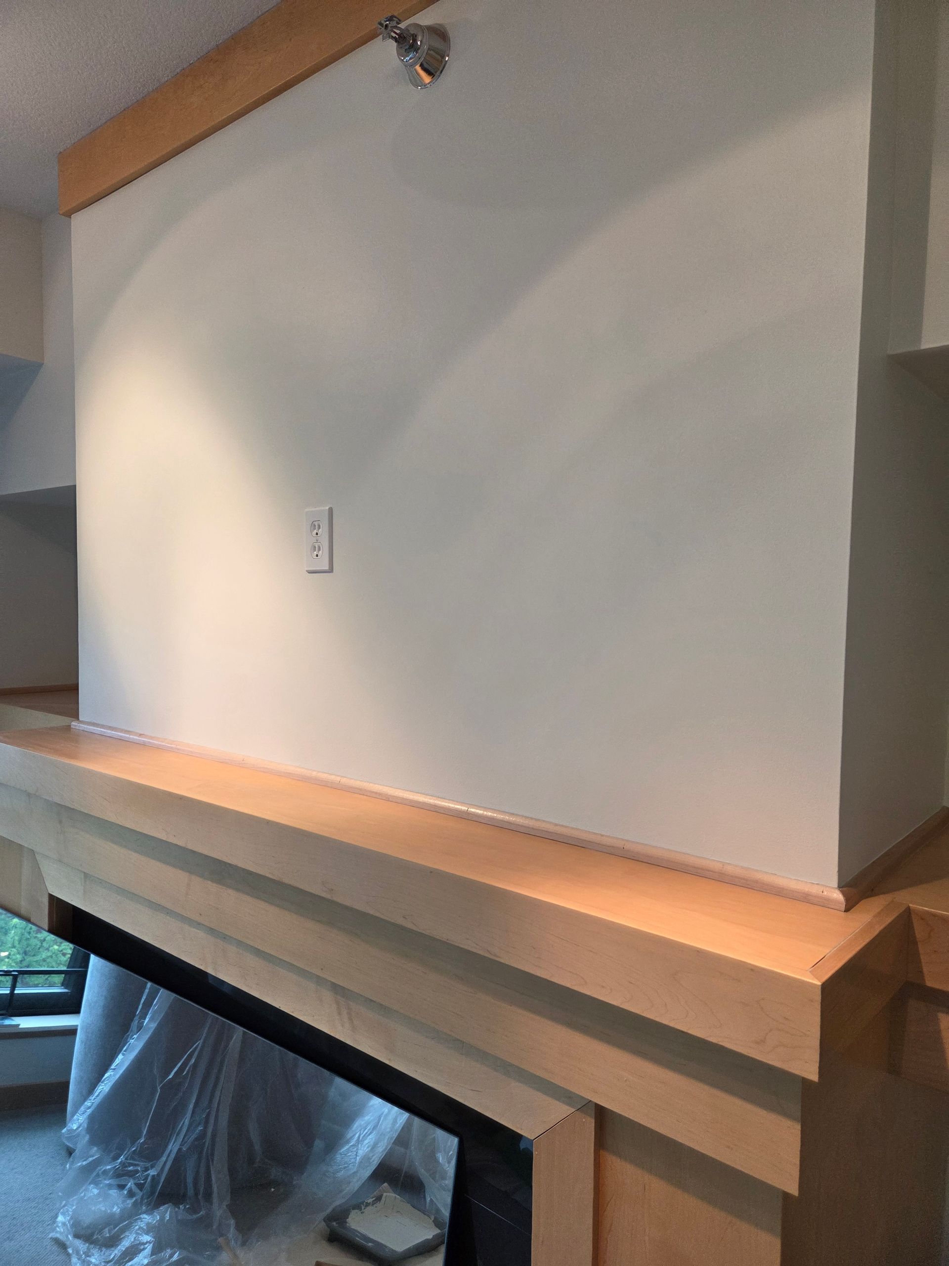 White wall above a beige mantel with wood trim and a small wall outlet in a room under construction