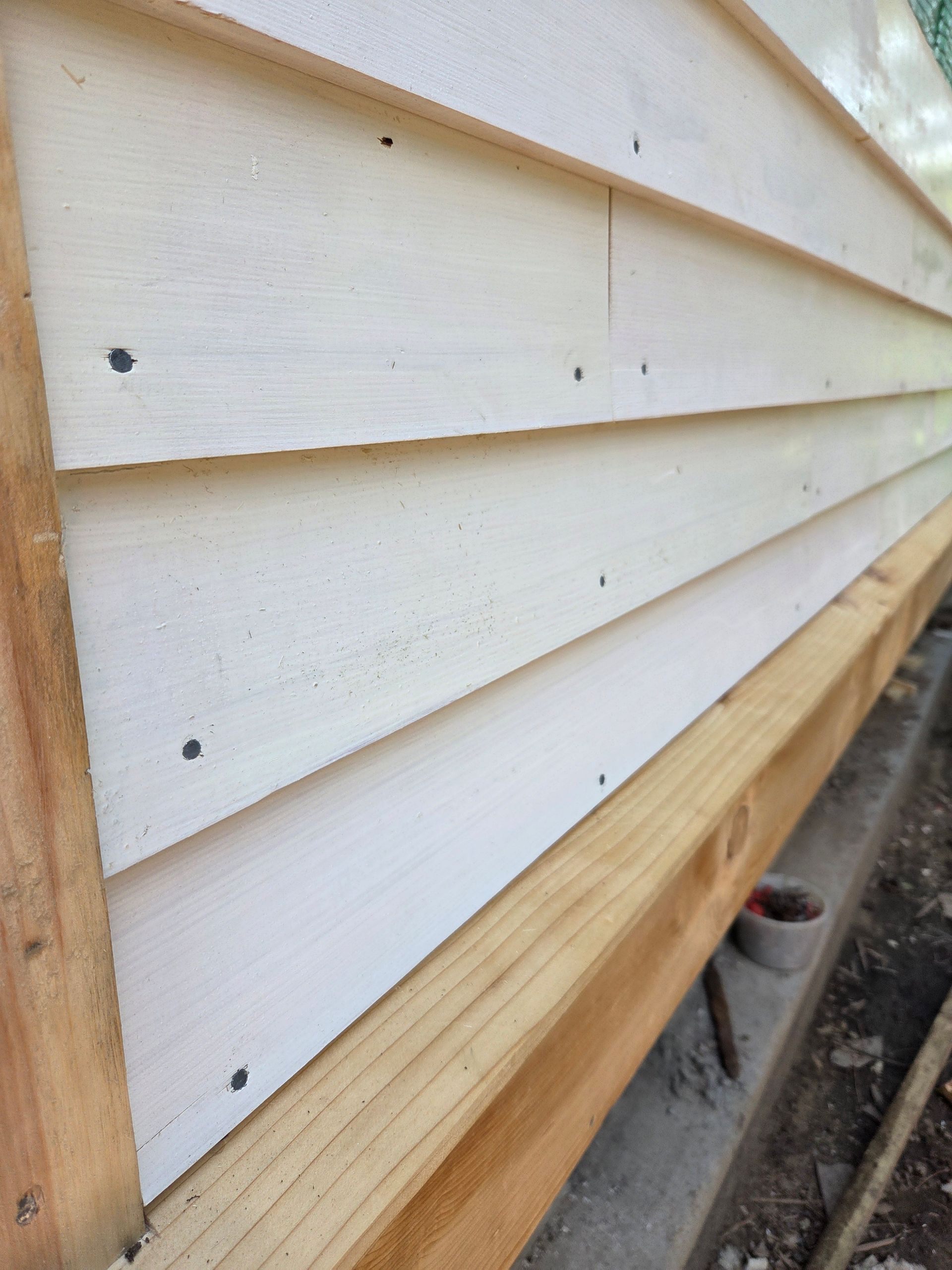 Close-up of white horizontal siding with wooden trim on a house exterior.