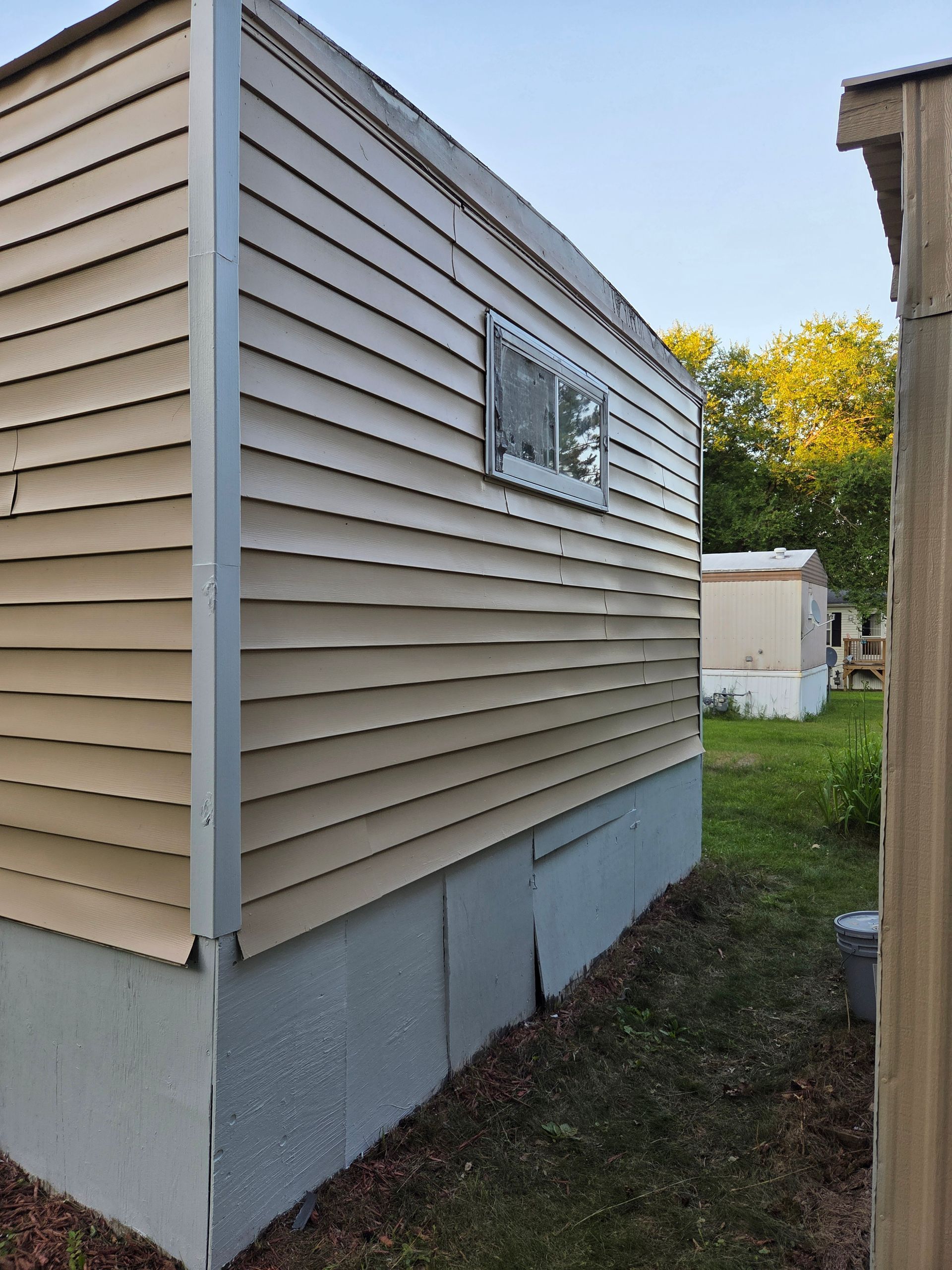 Side of a beige house with a small window, gray foundation, and a grassy yard beside a narrow walkway.