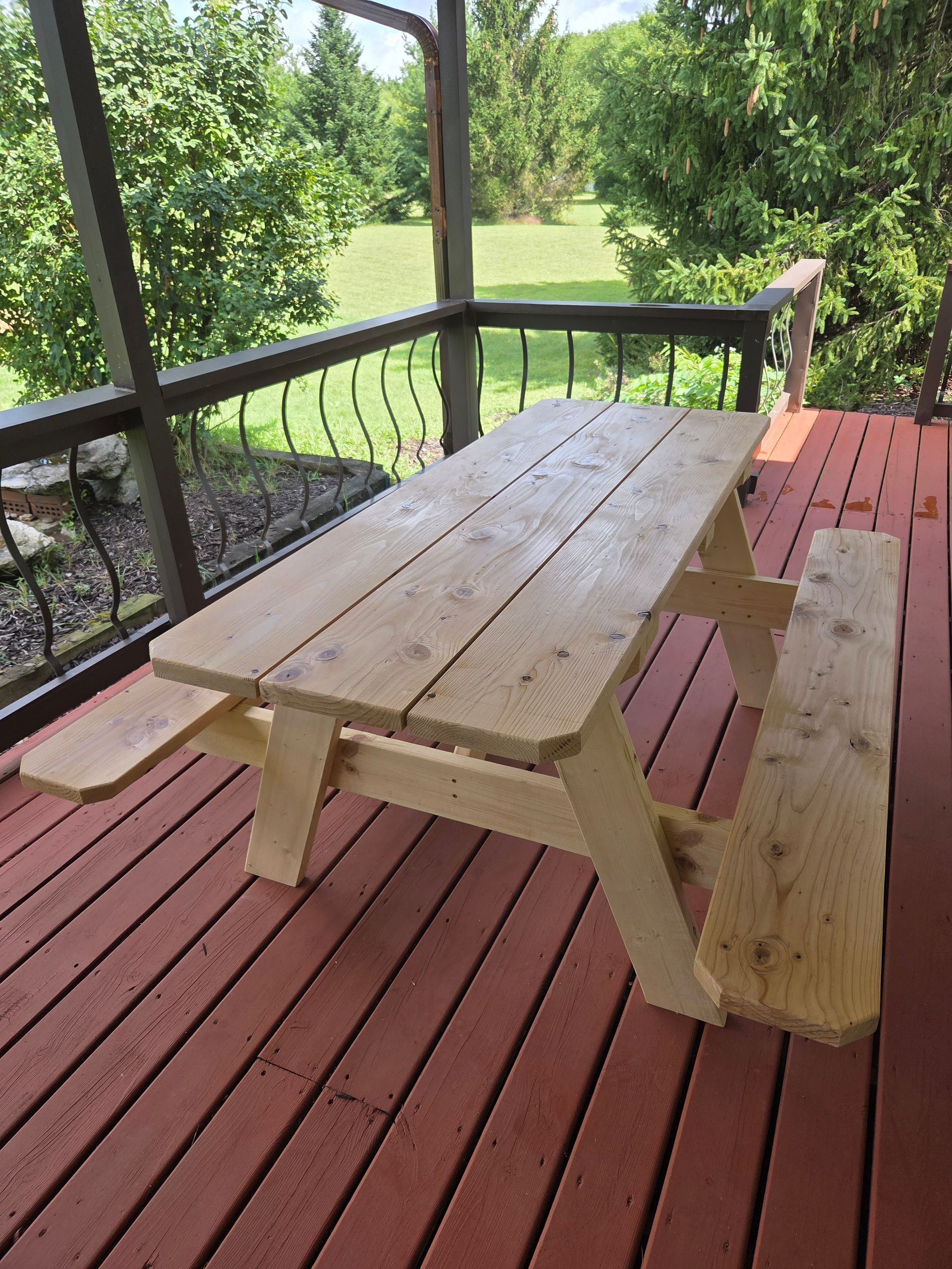 Wooden picnic table on a red deck overlooking a green yard and trees