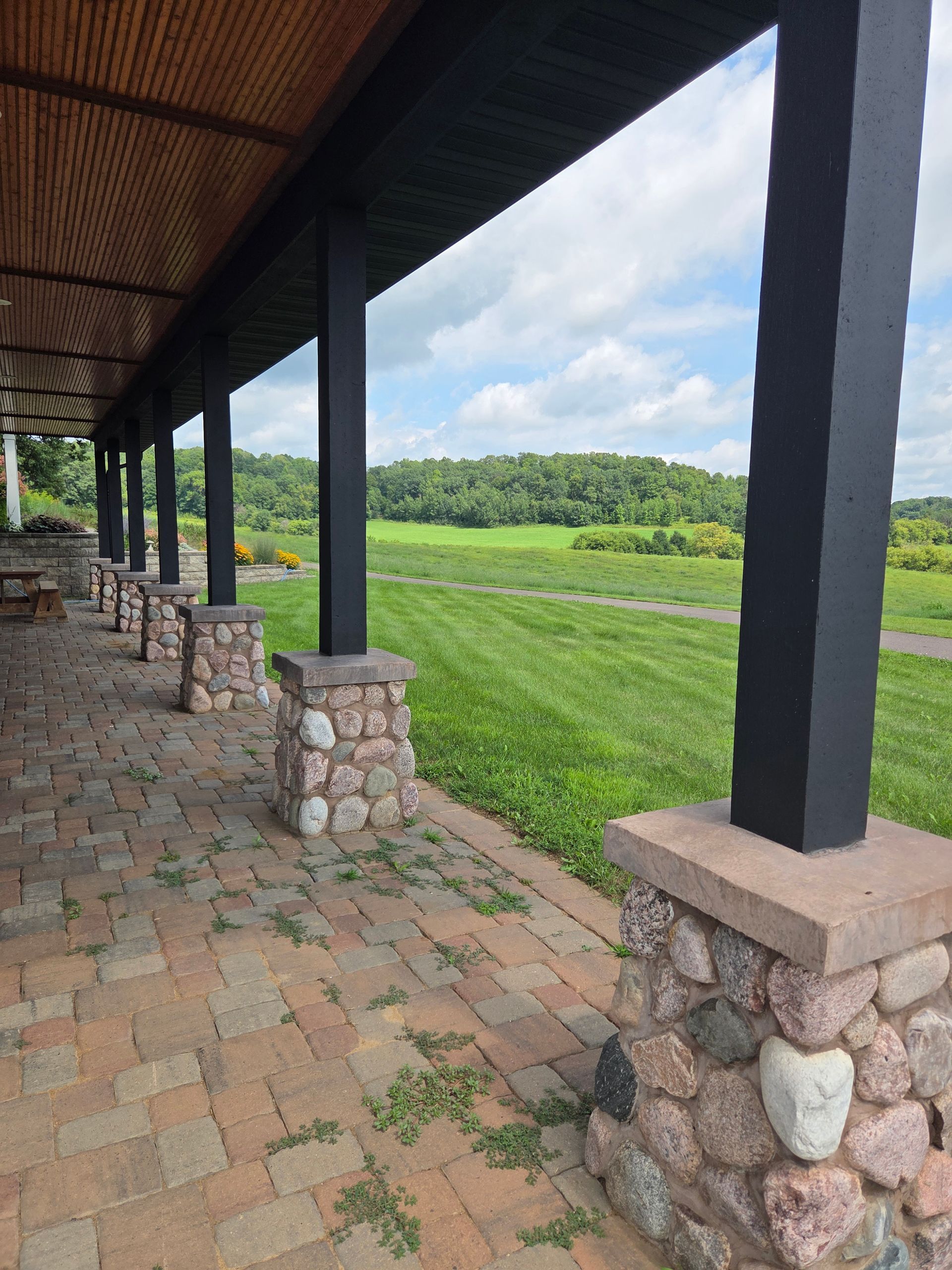 Covered stone walkway with black columns overlooking a green field and cloudy sky