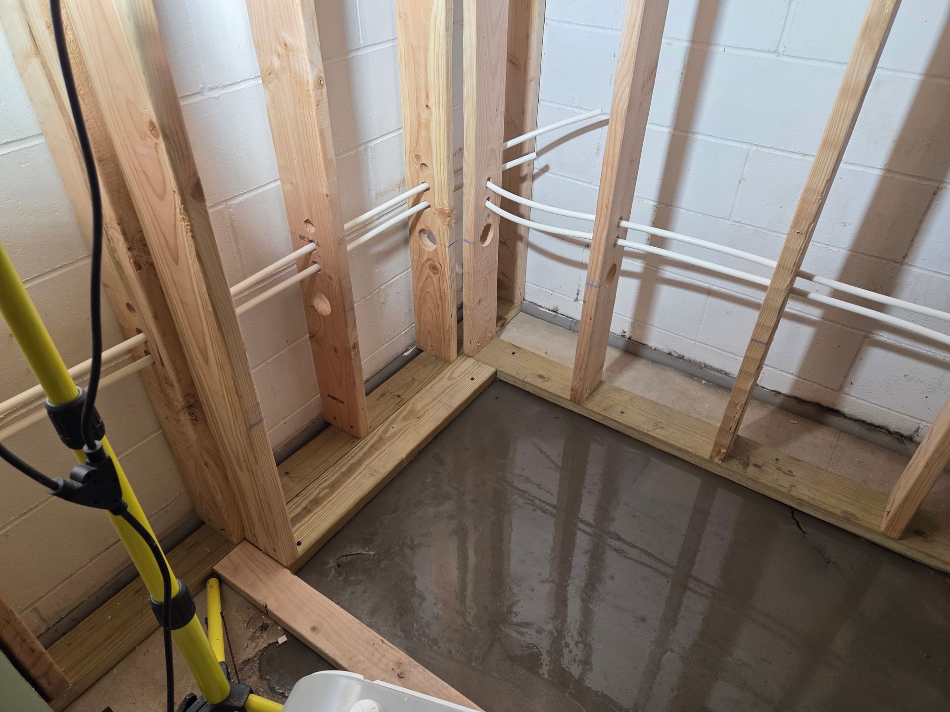 Framed basement wall corner with exposed studs and a freshly poured concrete floor