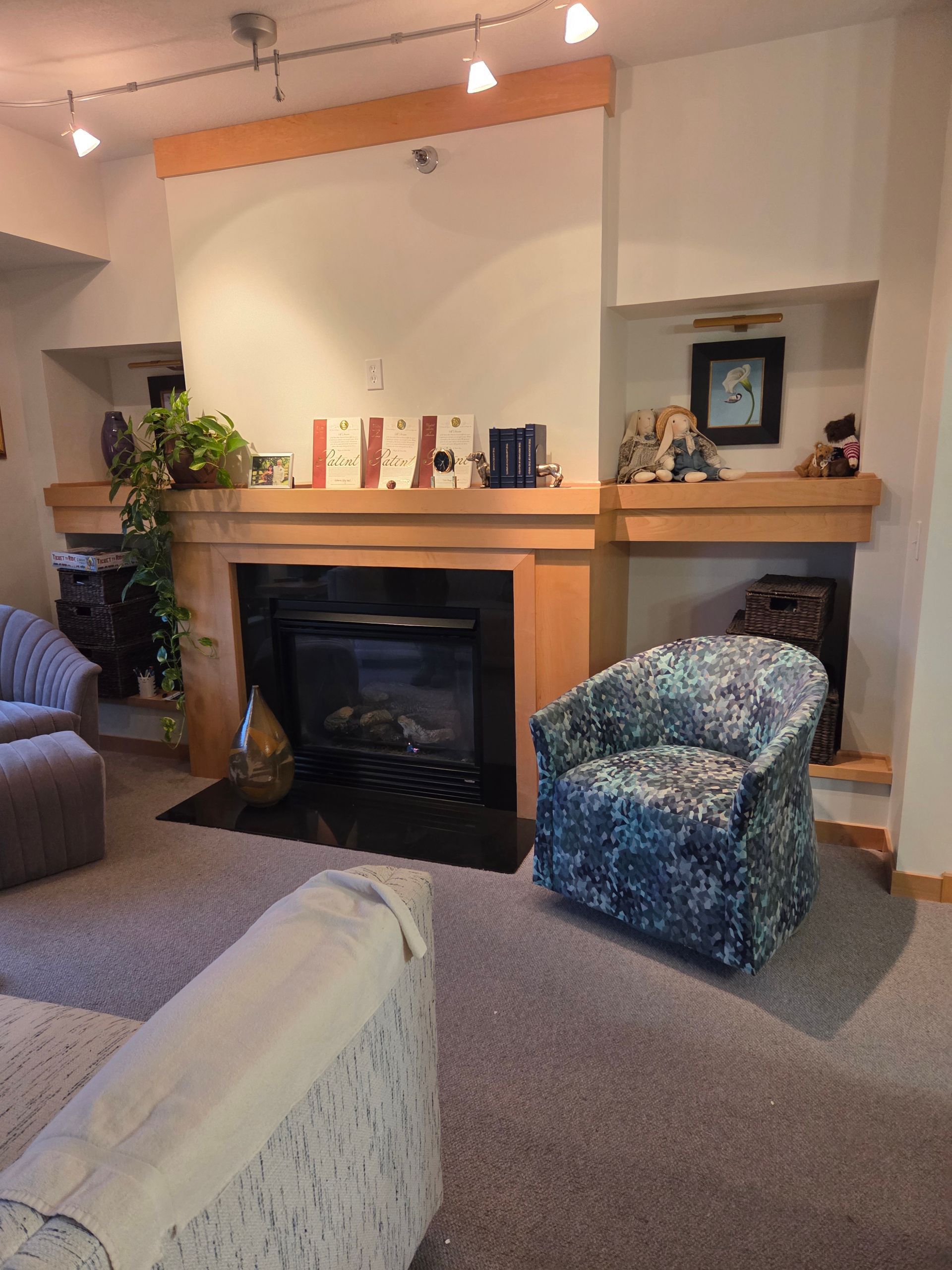 Cozy living room with a fireplace, wooden mantel, blue patterned armchair, and soft lighting.