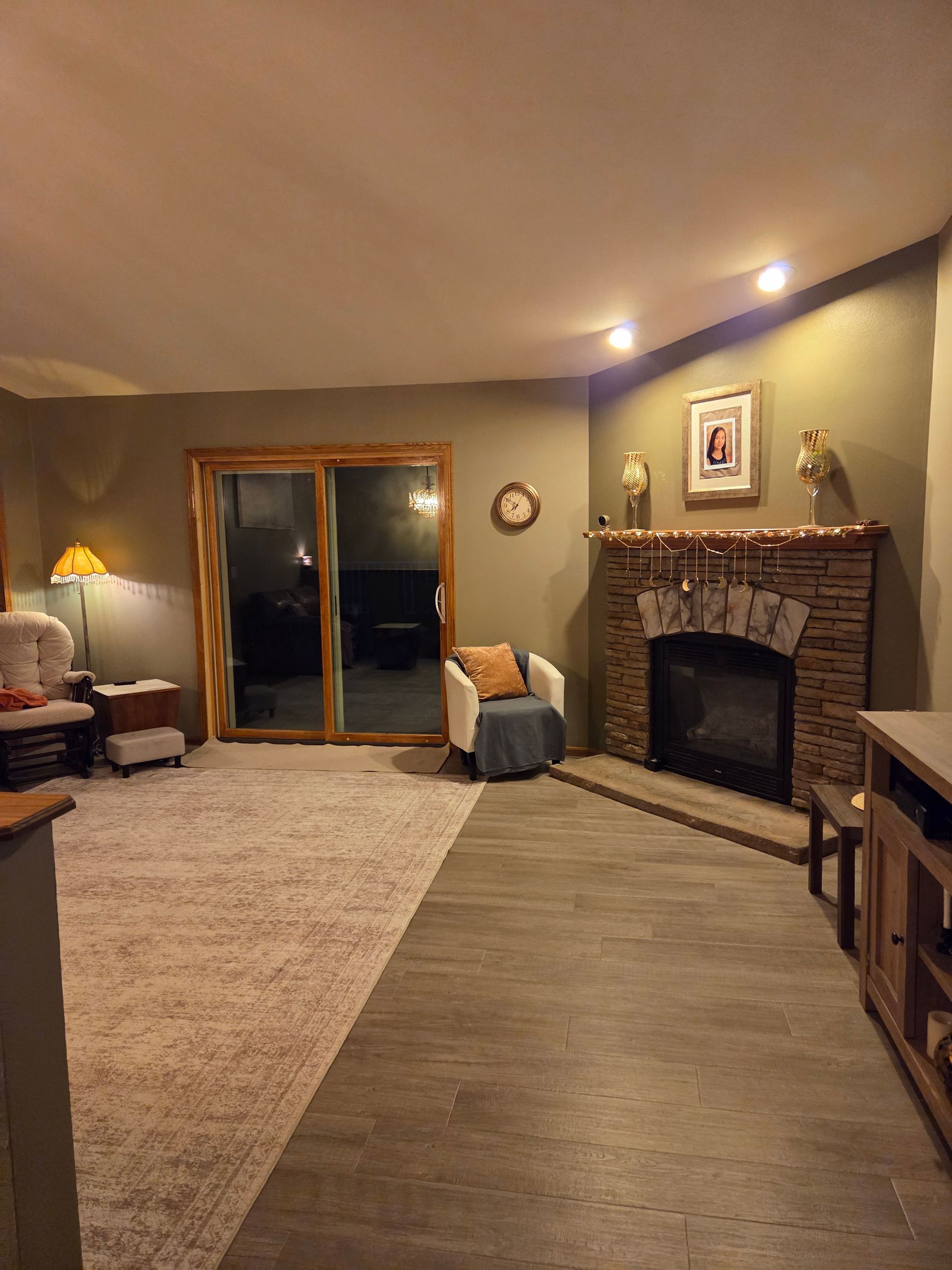 Living room with fireplace, sliding glass doors, rug, and lamp in warm lighting