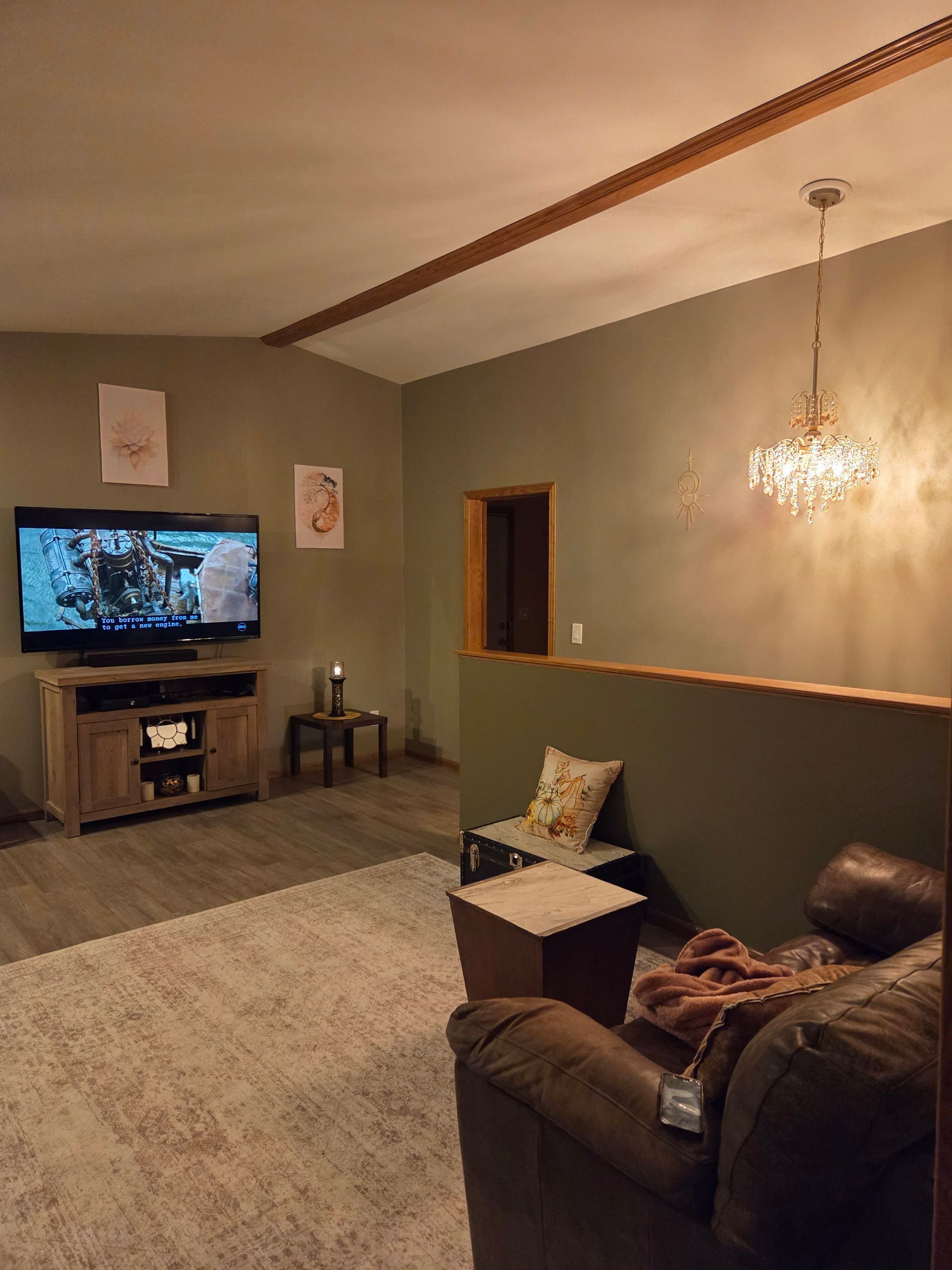 Living room with a TV, sofa, chandelier, and warm beige walls with wood trim