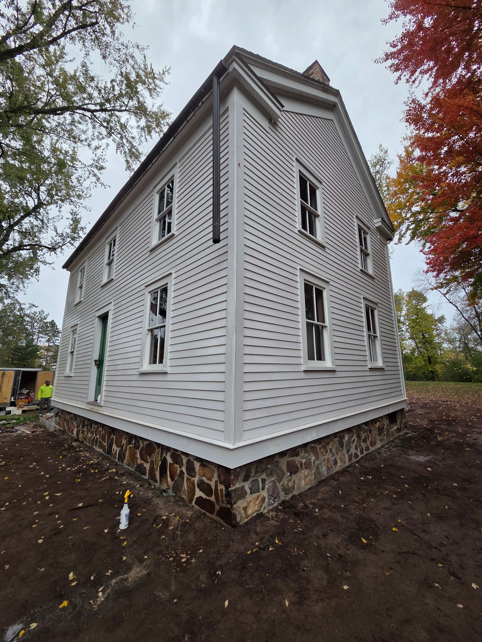 White clapboard house exterior with tall windows, viewed from the corner amid autumn trees