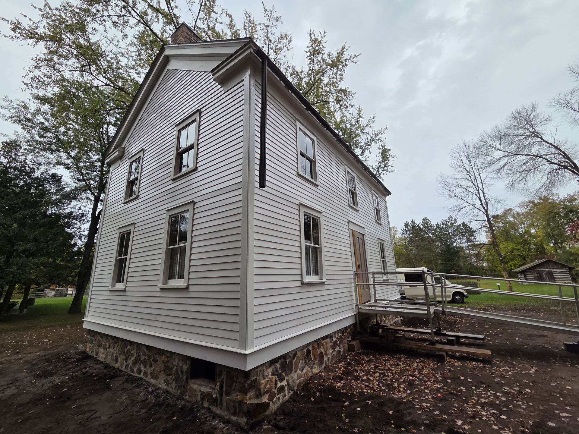 White house with gray trim on a raised foundation, viewed from the corner in a wooded yard.