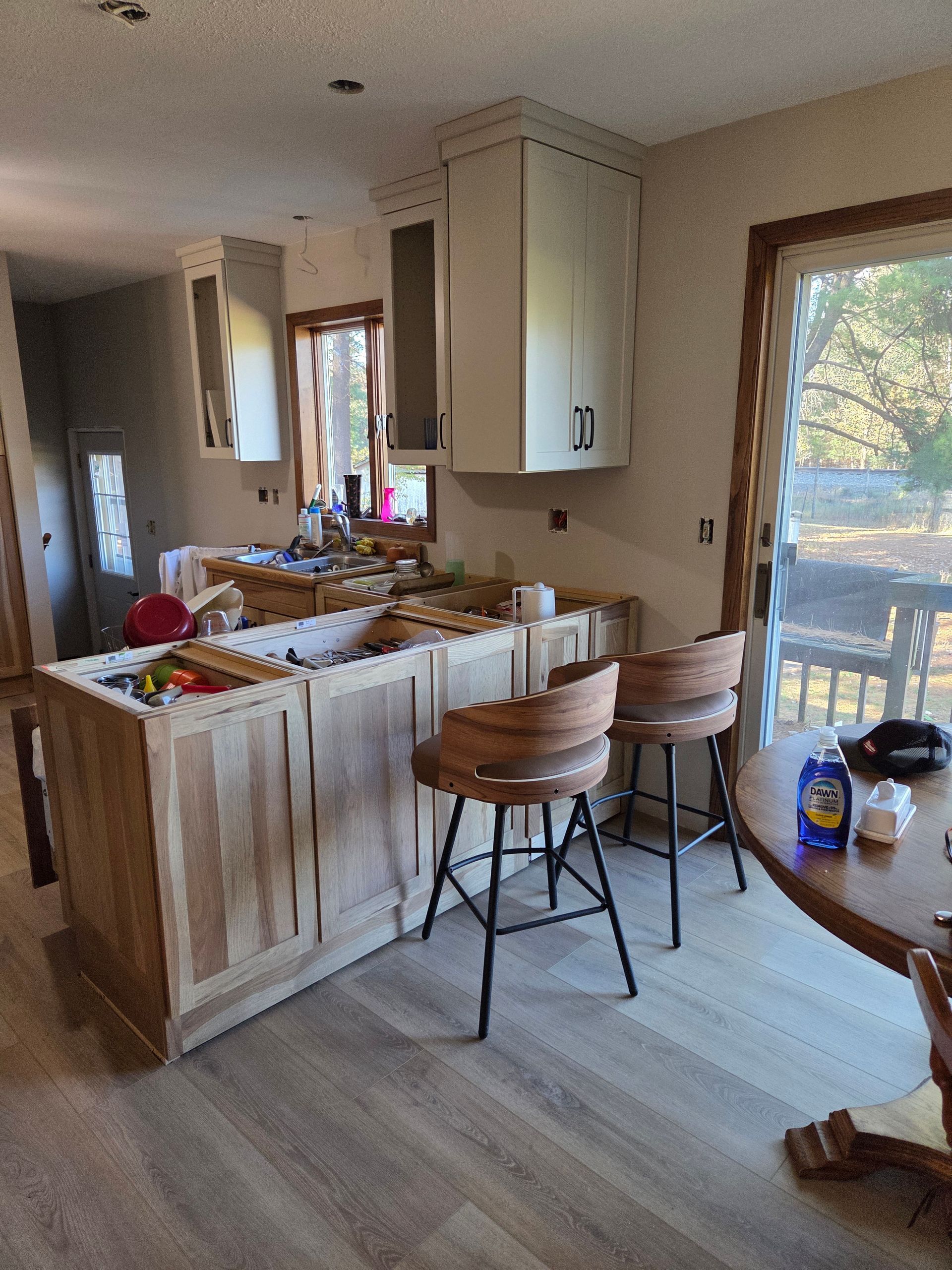 Kitchen with island cluttered with items, bar stools, and sliding glass door to a sunny patio outside.