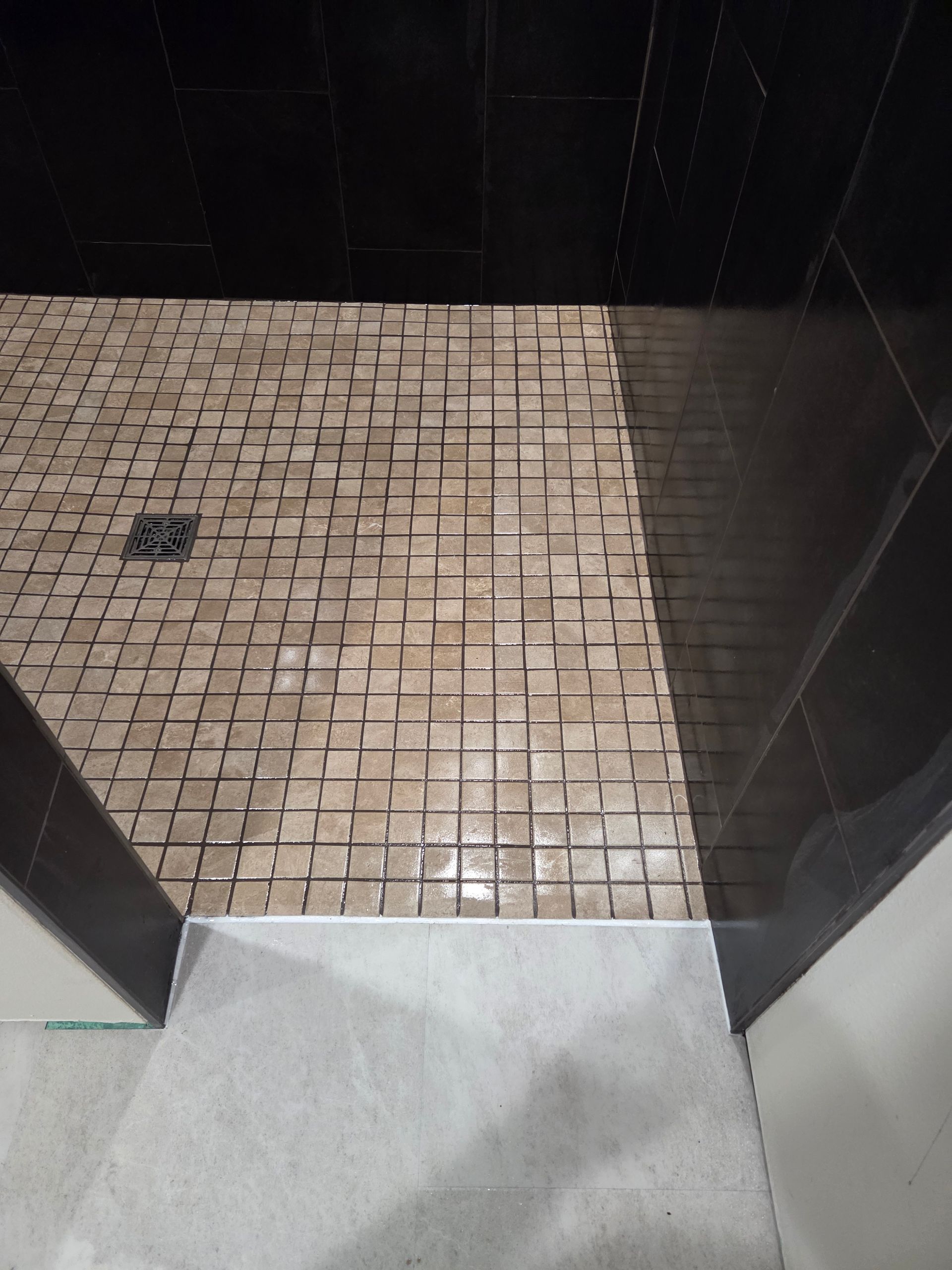 Small tiled shower area with a drain and dark walls, viewed from the doorway