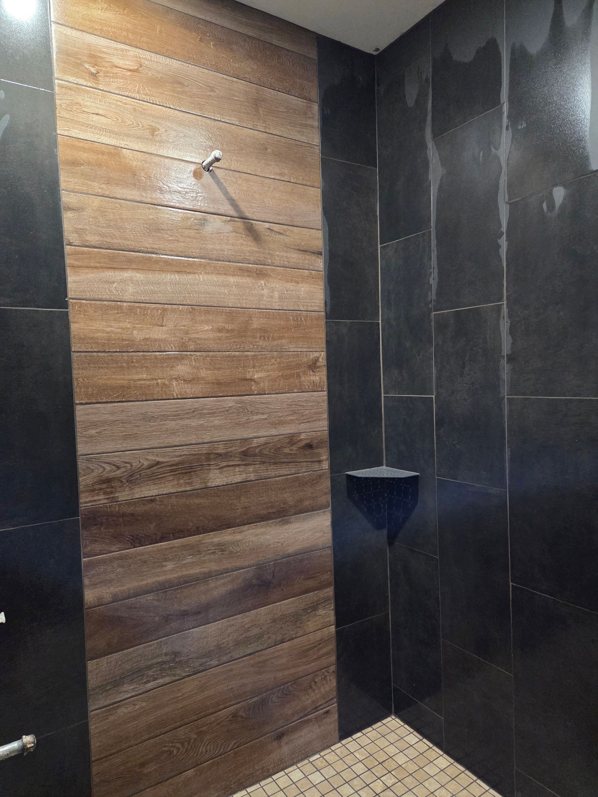Modern bathroom shower with wood-look and dark tile walls, glass partition, and built-in corner shelf