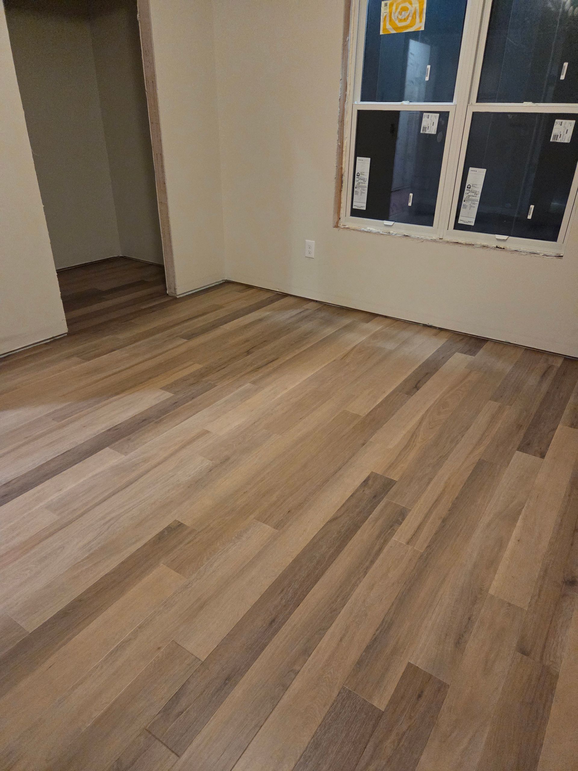 Empty room with wood flooring, beige walls, and a window near an open doorway.