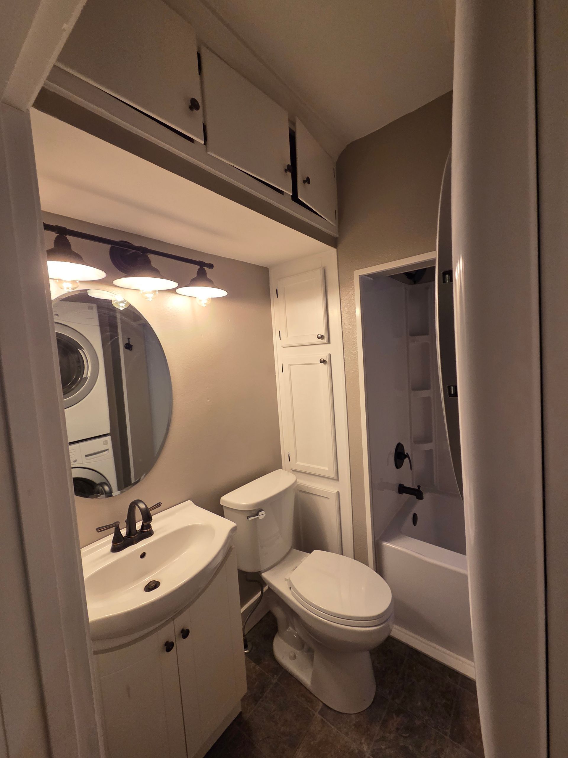 Small bathroom with sink, toilet, mirror, cabinet, and shower stall in a narrow beige space.