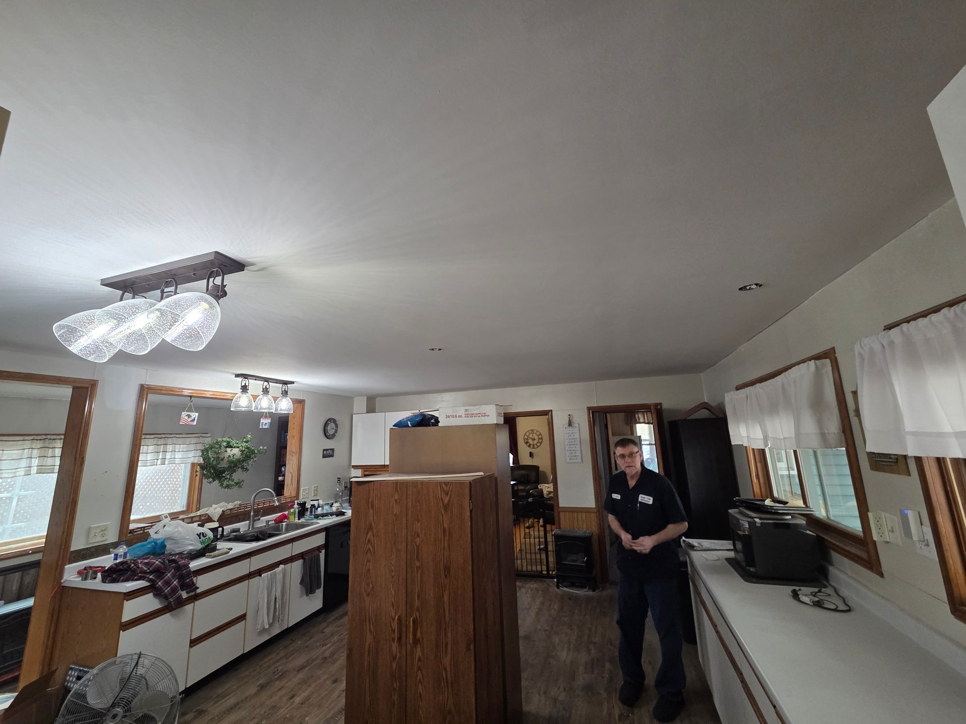 Wide kitchen with white cabinets and countertops; a person stands near the doorway in a bright home interior.