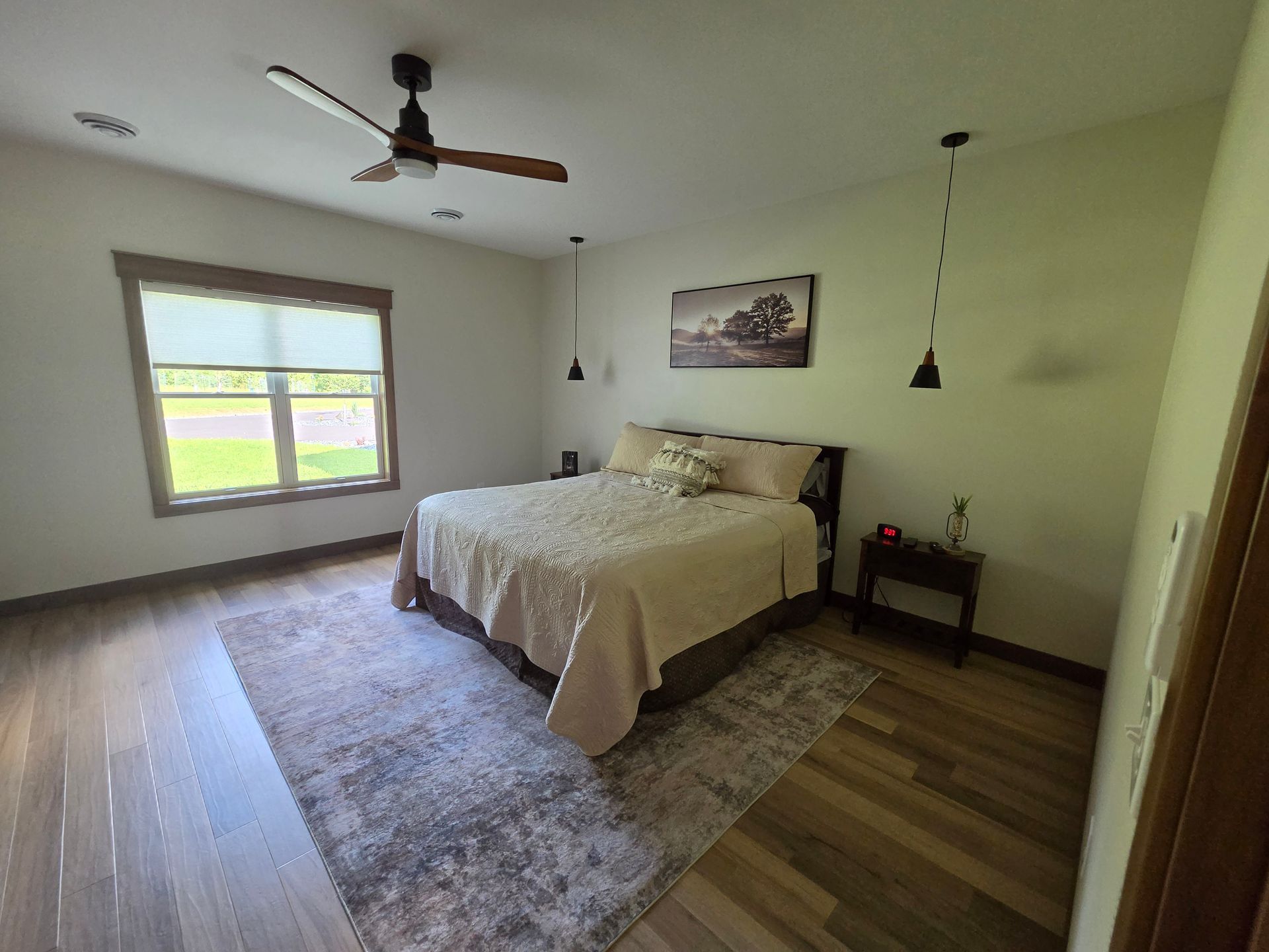 Bright bedroom with a bed, rug, ceiling fan, and window overlooking a green field.