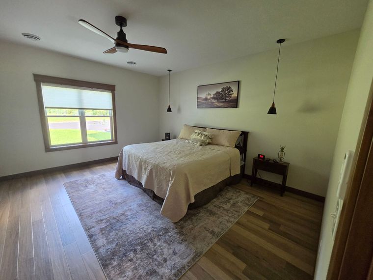 Bright bedroom with a bed, rug, ceiling fan, and window overlooking a green field.
