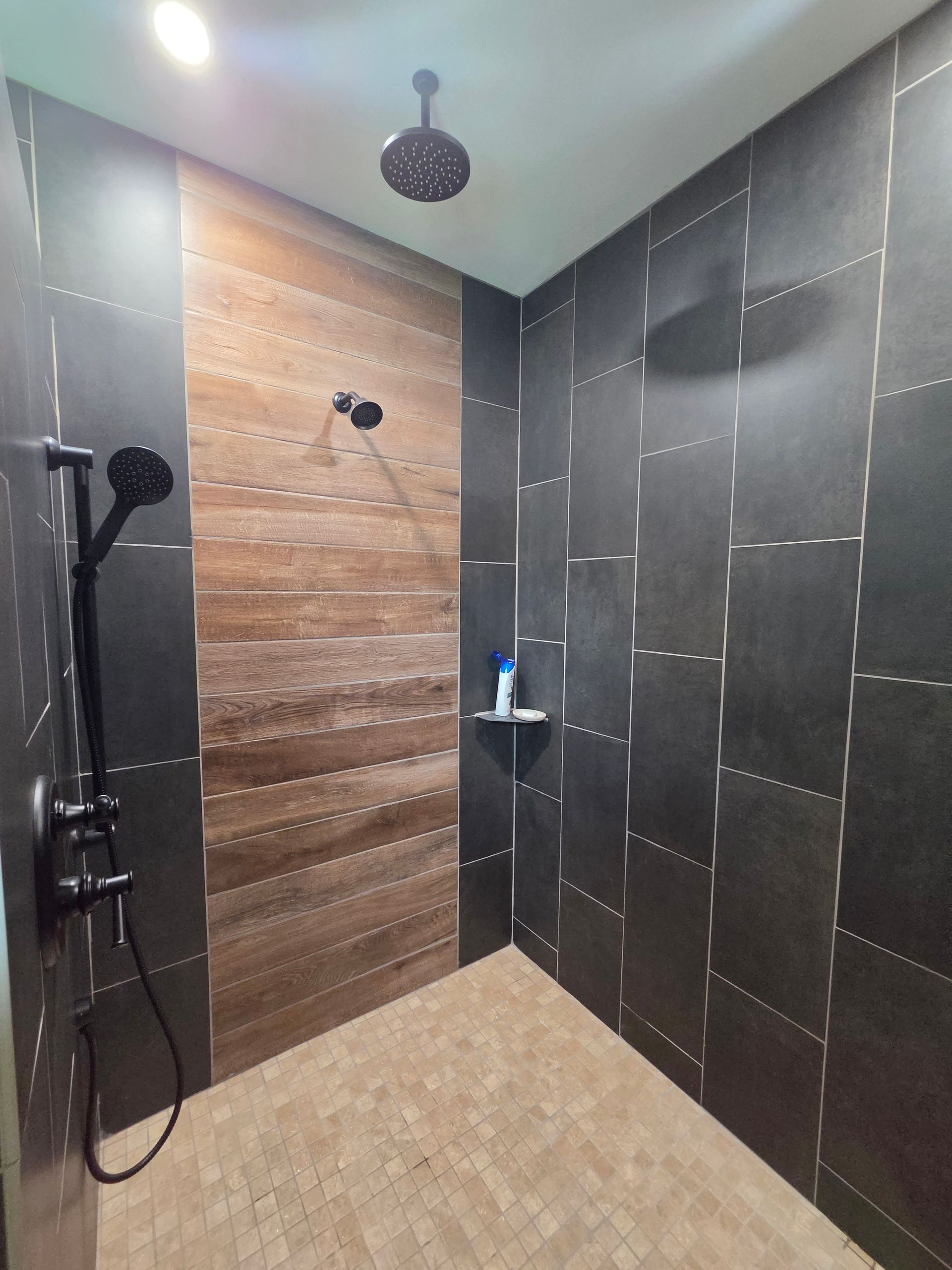 Modern tiled walk-in shower with black walls, beige floor, and a rainfall showerhead