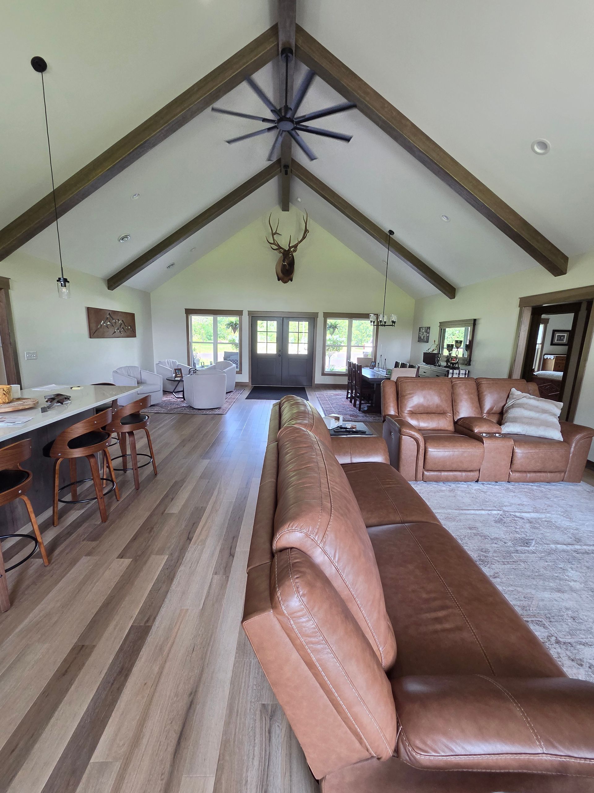 Spacious living room with leather sofas, bar stools, vaulted ceiling, and ceiling fan.