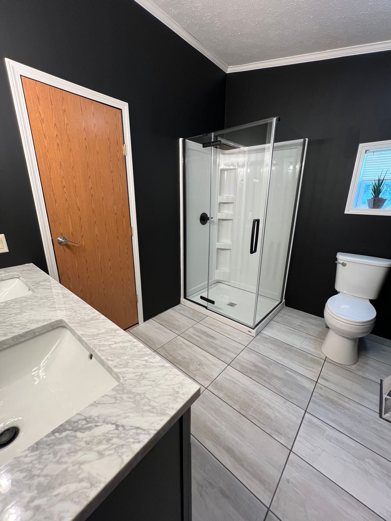 Small bathroom with walk-in shower, toilet, sink, dark walls, and gray tile floor.
