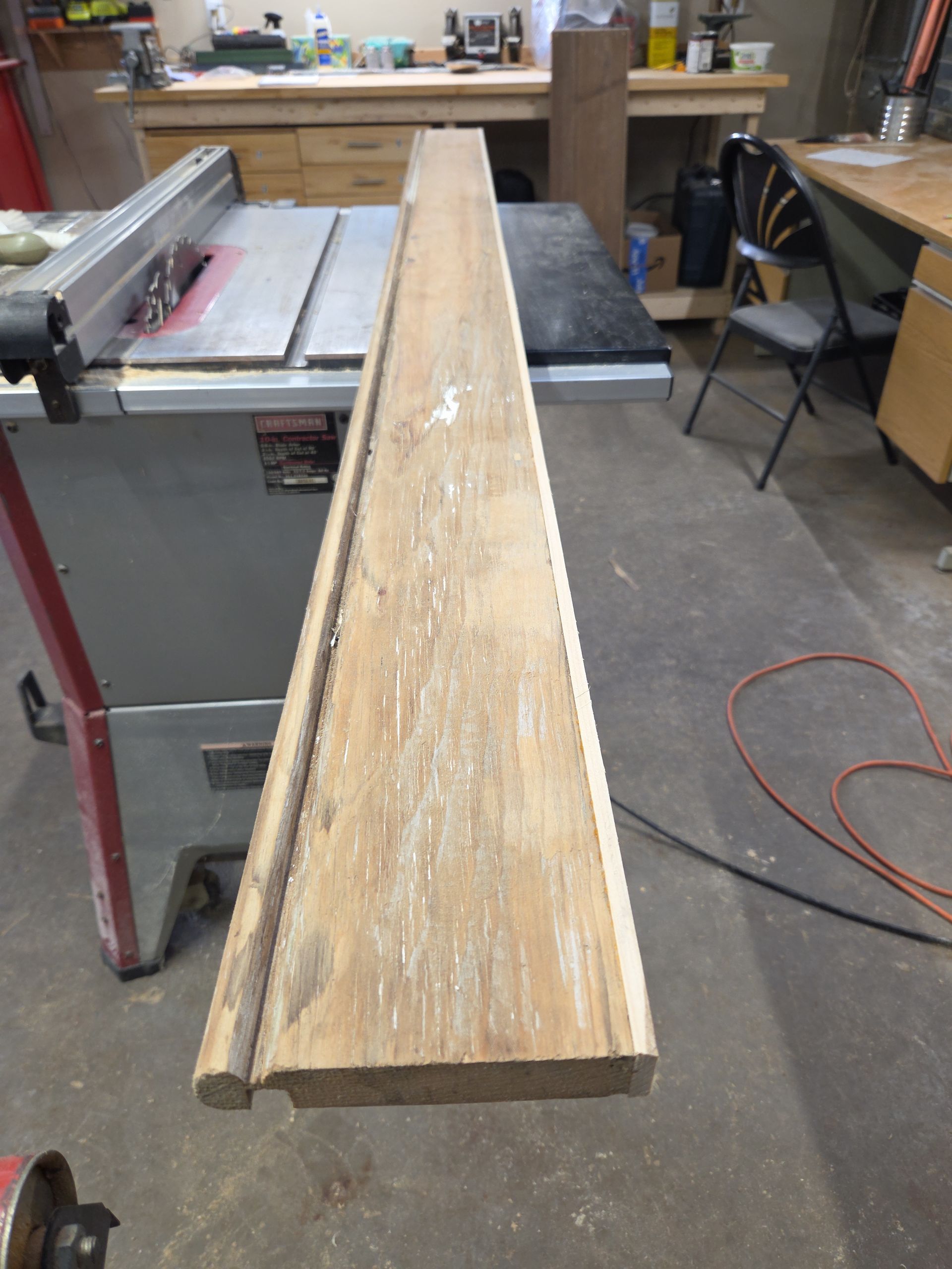 Long weathered wooden plank resting across a table saw in a workshop