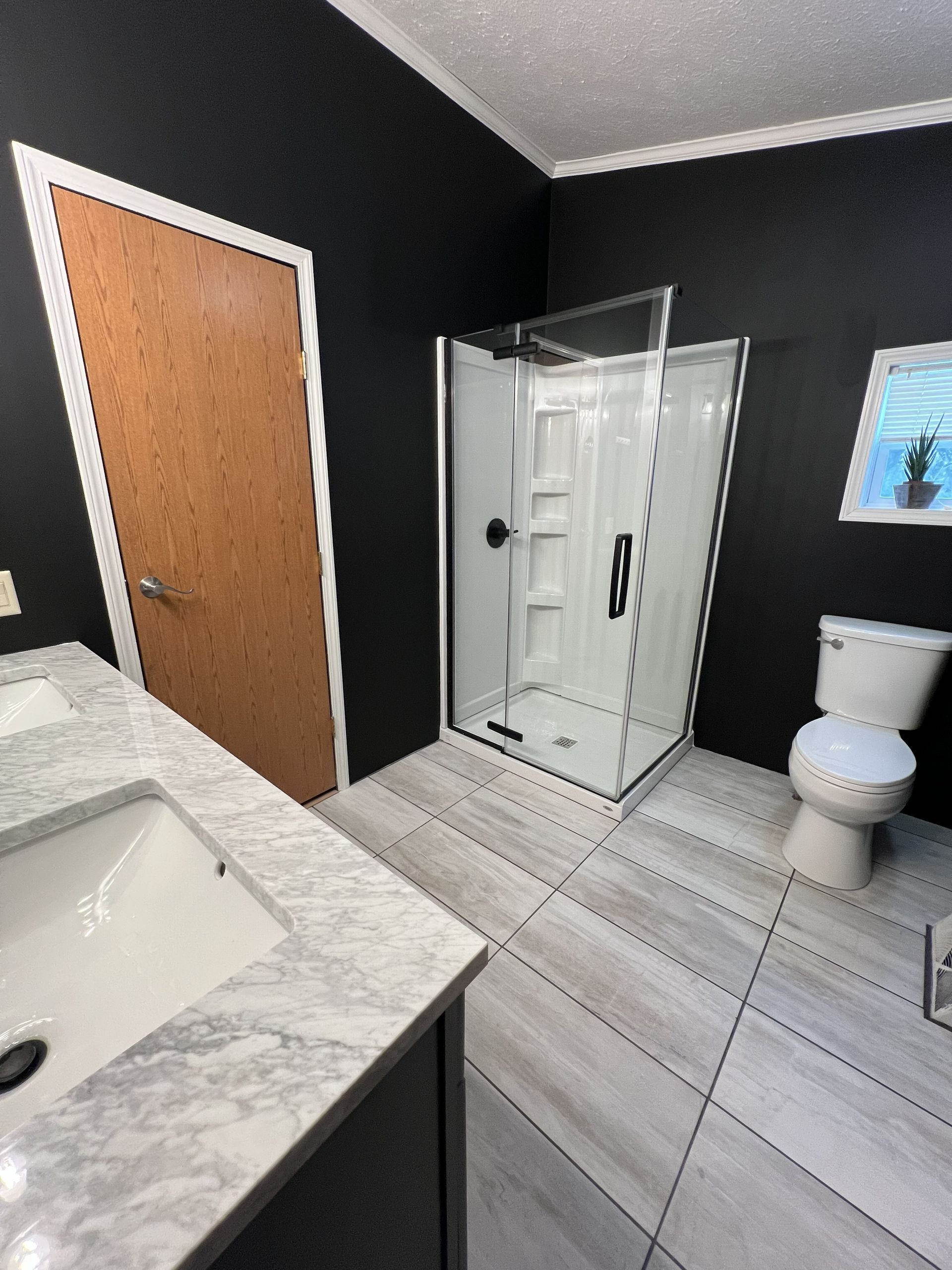 Bathroom with black walls, white tile floor, glass shower, toilet, and vanity with sink.