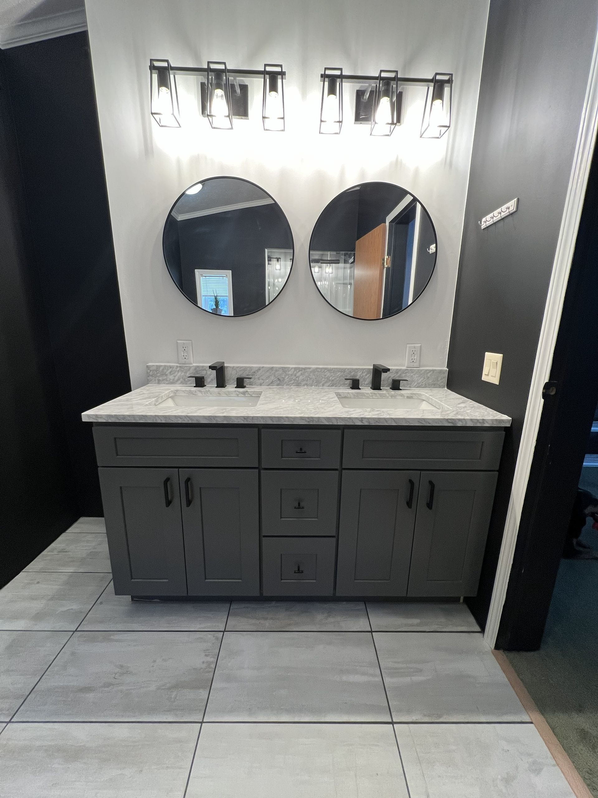 Modern double vanity with two round mirrors and wall sconces in a tiled bathroom.