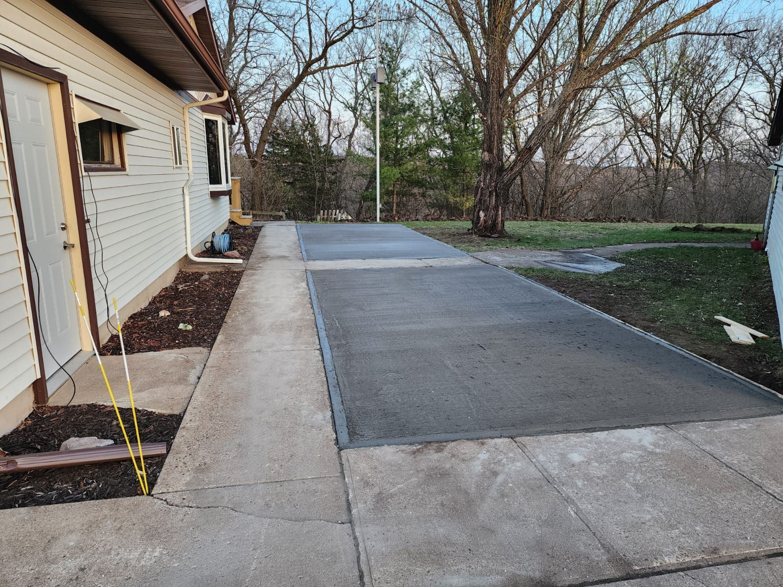 Concrete driveway beside a house, with a darker resurfaced section and trees in the background