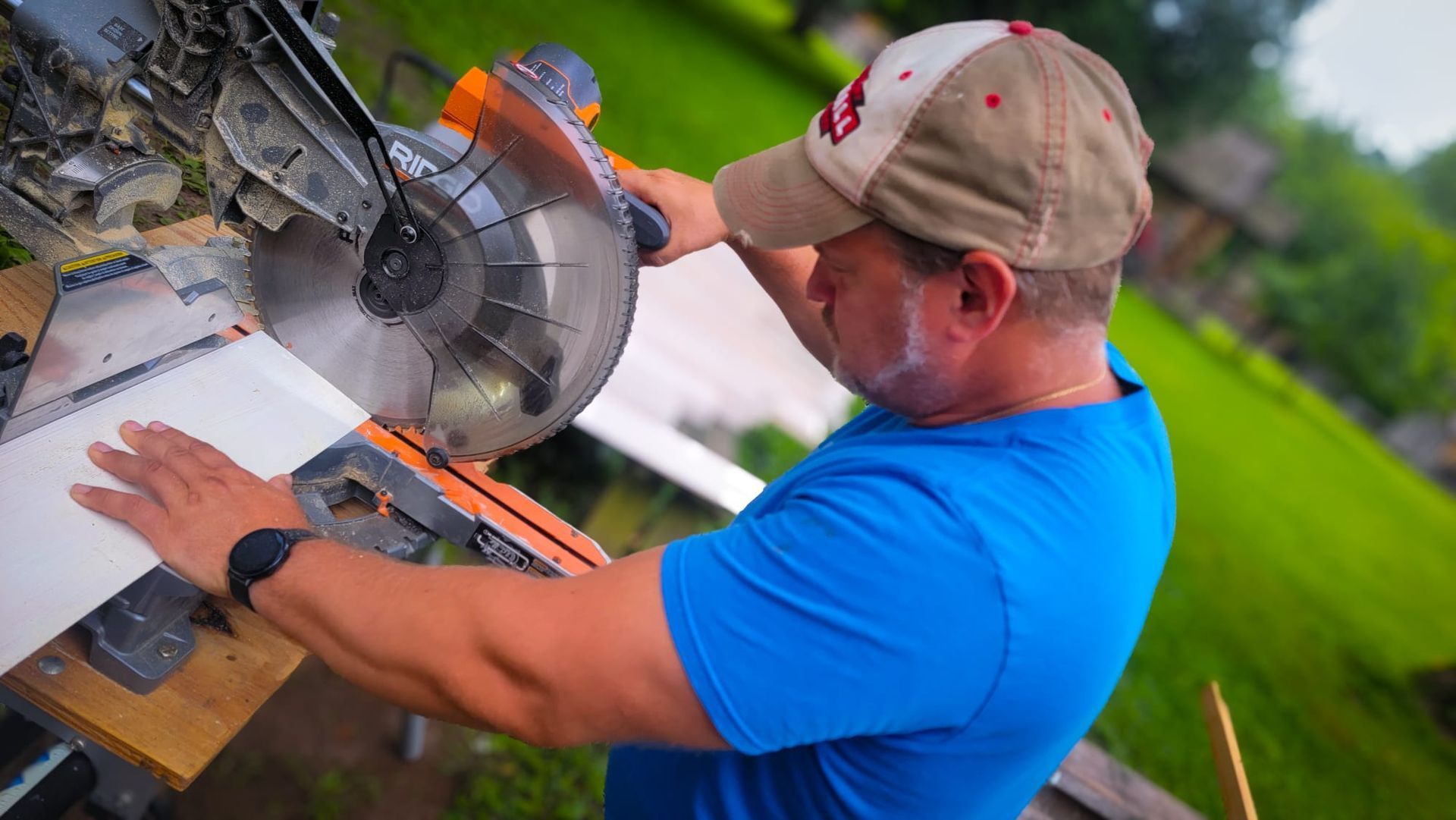 Worker in blue shirt operating a miter saw outdoors on a workbench