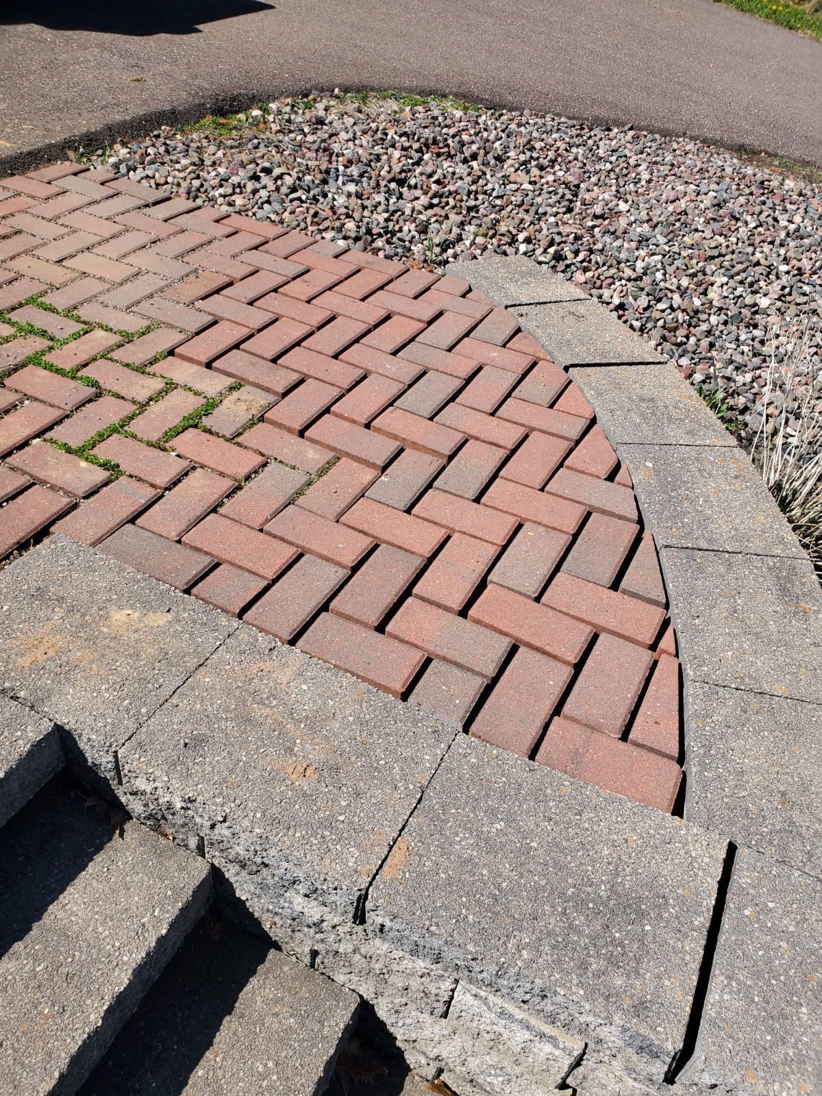 Curved brick walkway with a concrete border beside a gravel bed and steps.