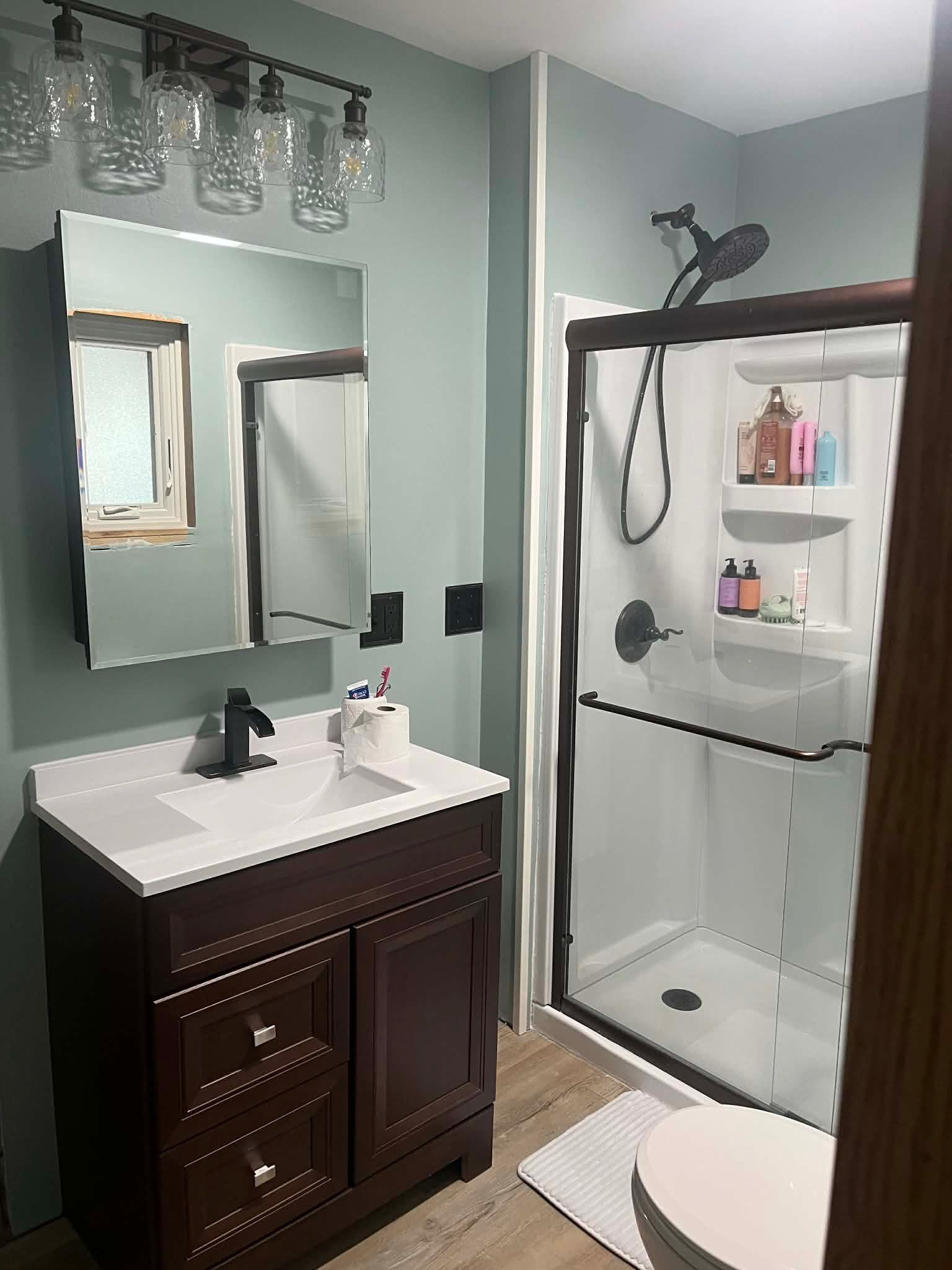 Small bathroom with dark vanity, white sink, mirror, glass shower, and mint green walls.