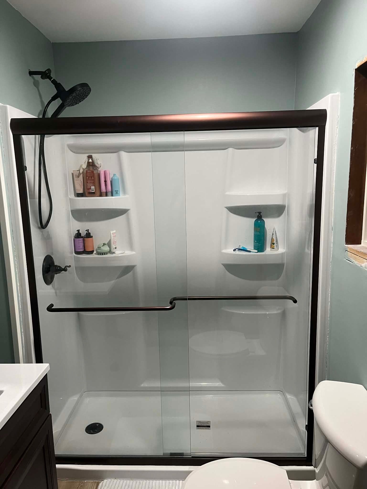 Walk-in shower with white tile, glass doors, built-in shelves, and black fixtures in a gray bathroom.