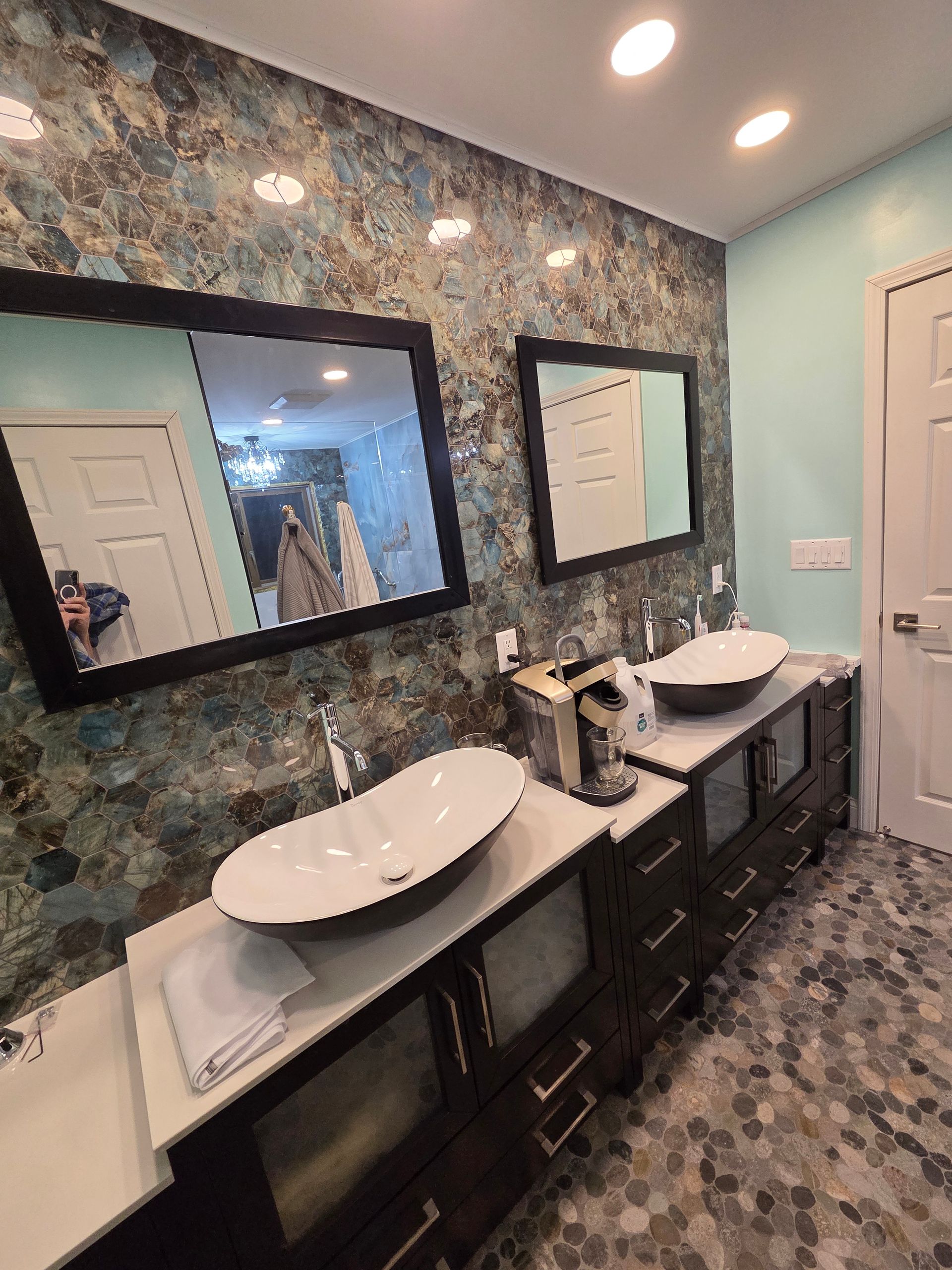 Modern bathroom with double sinks, large mirror, patterned blue-green wall, and marble-look floor tiles