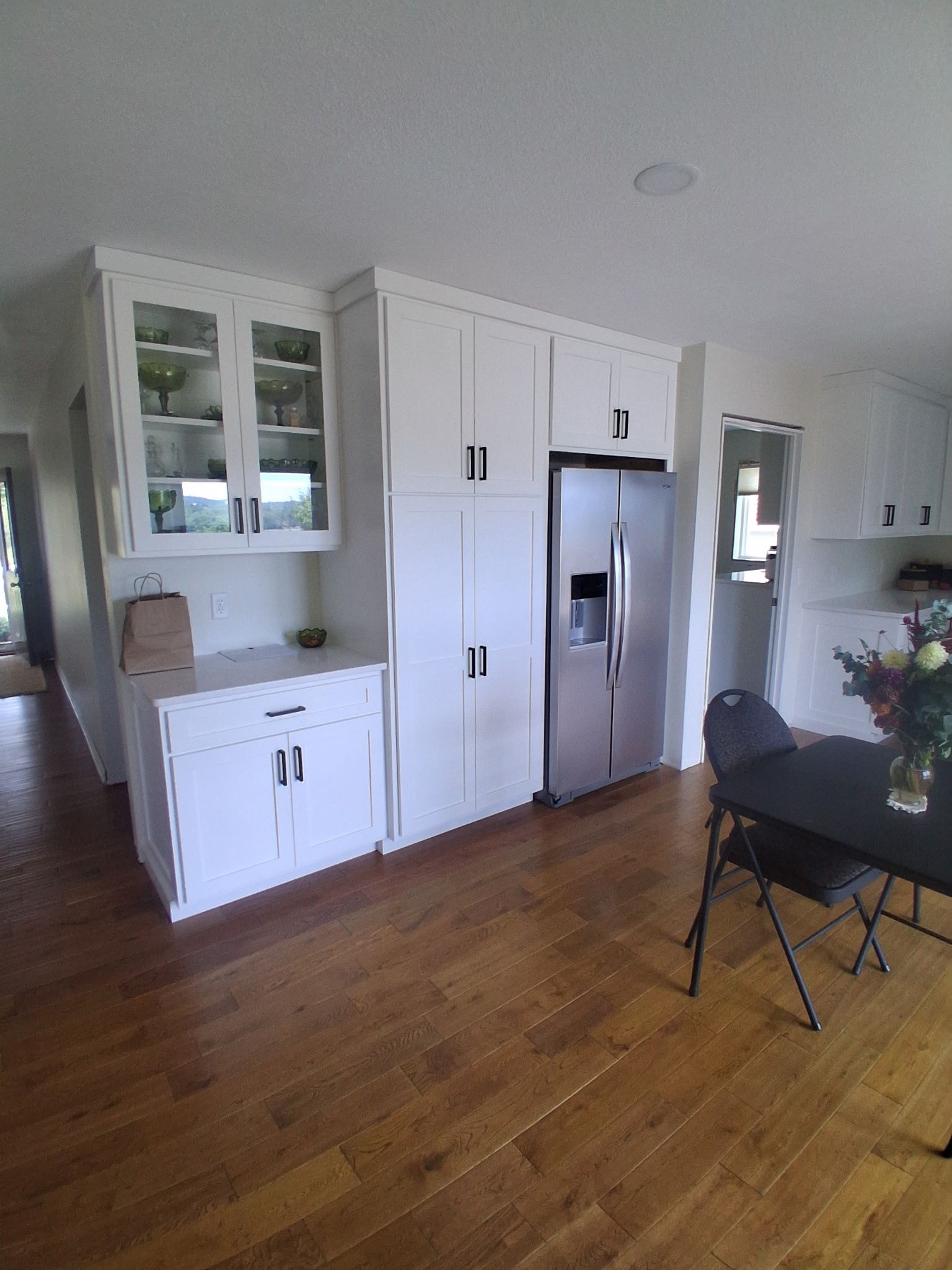 Bright kitchen with white cabinets, stainless fridge, hardwood floor, and a small table and chairs