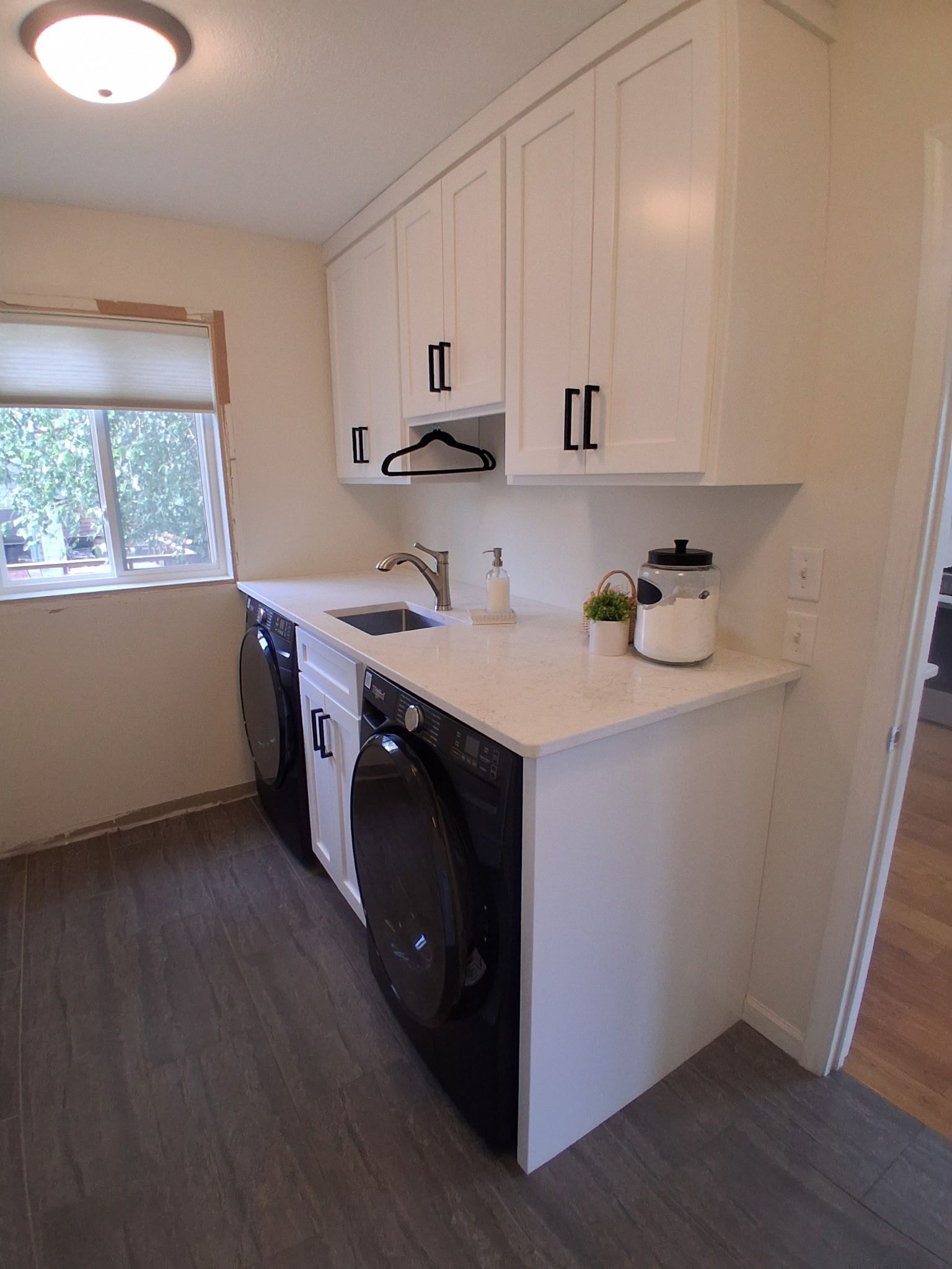 Bright laundry room with white cabinets, stacked washer and dryer, and a window on the left.