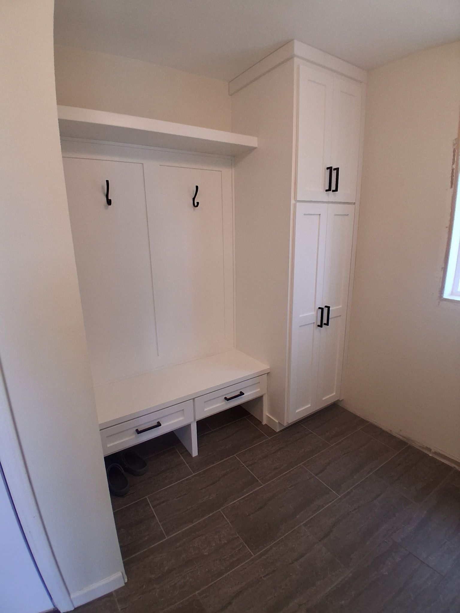 Empty beige mudroom with white built-in cabinets and bench seating.
