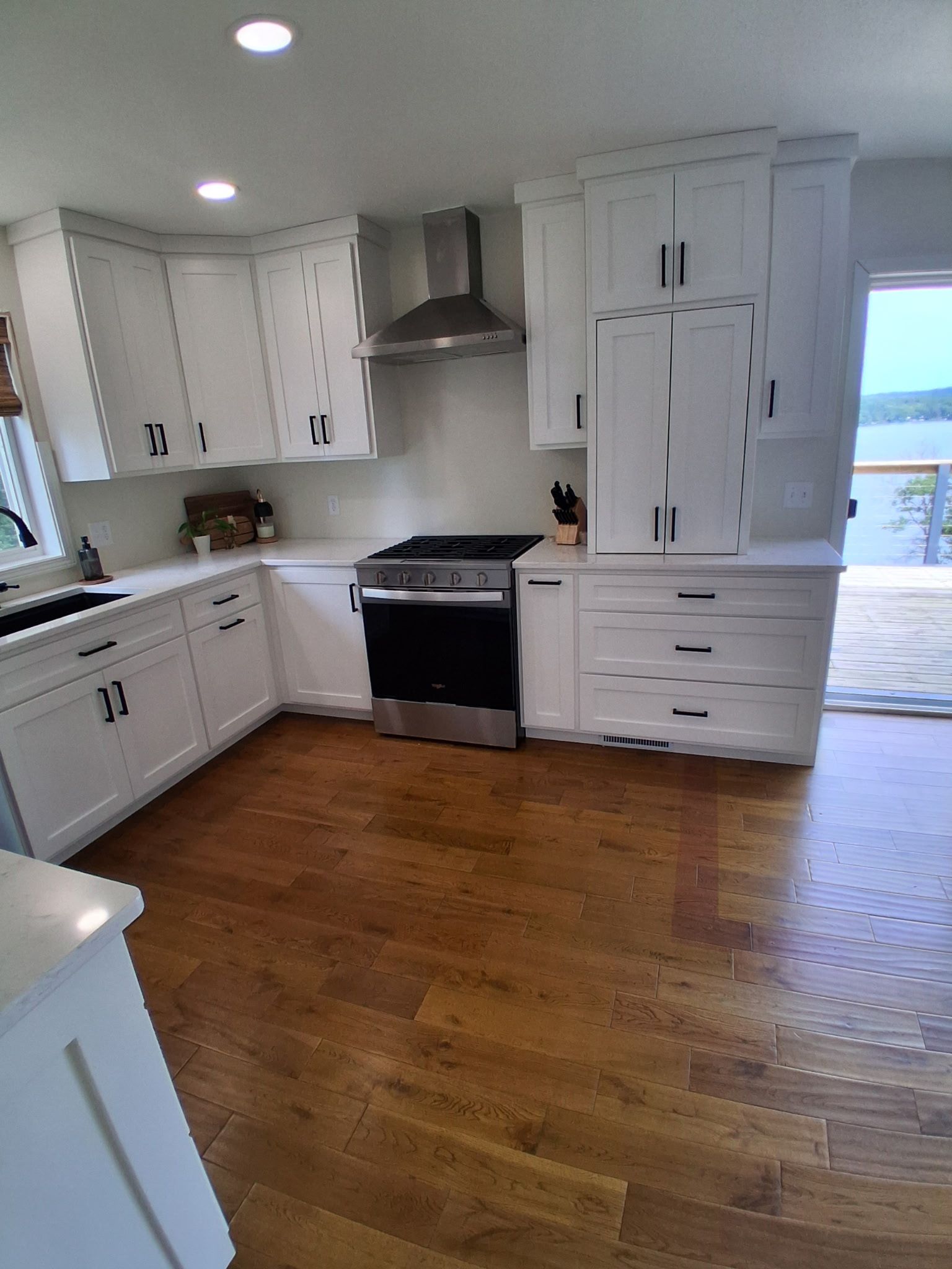 Bright white kitchen with black stove, wood floor, and a doorway to a lake view.