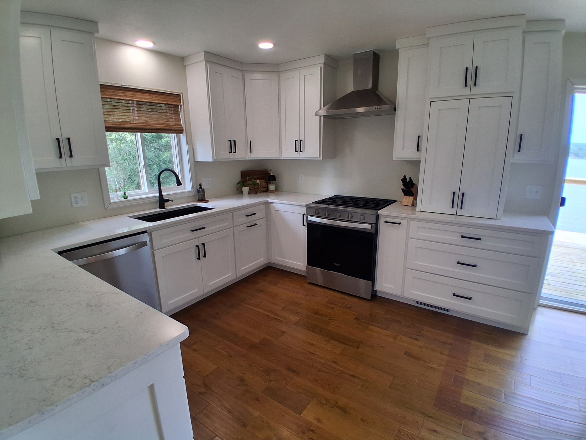 Bright white kitchen with cabinets, stainless stove, window over sink, and hardwood floor.