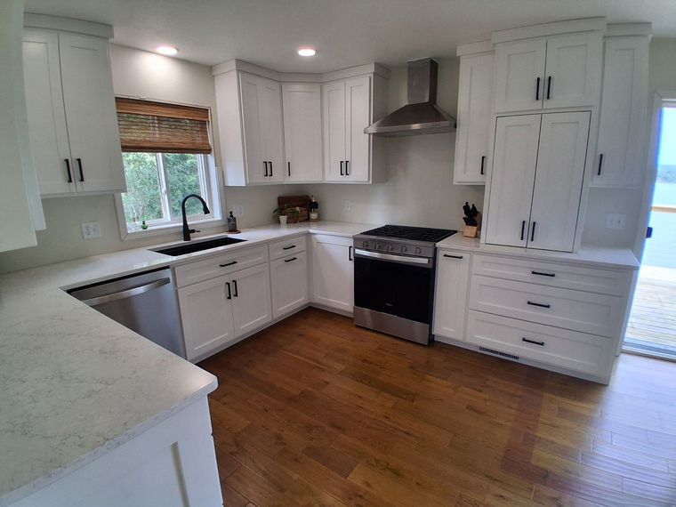 Bright white kitchen with L-shaped cabinets, stainless range hood, and hardwood floors