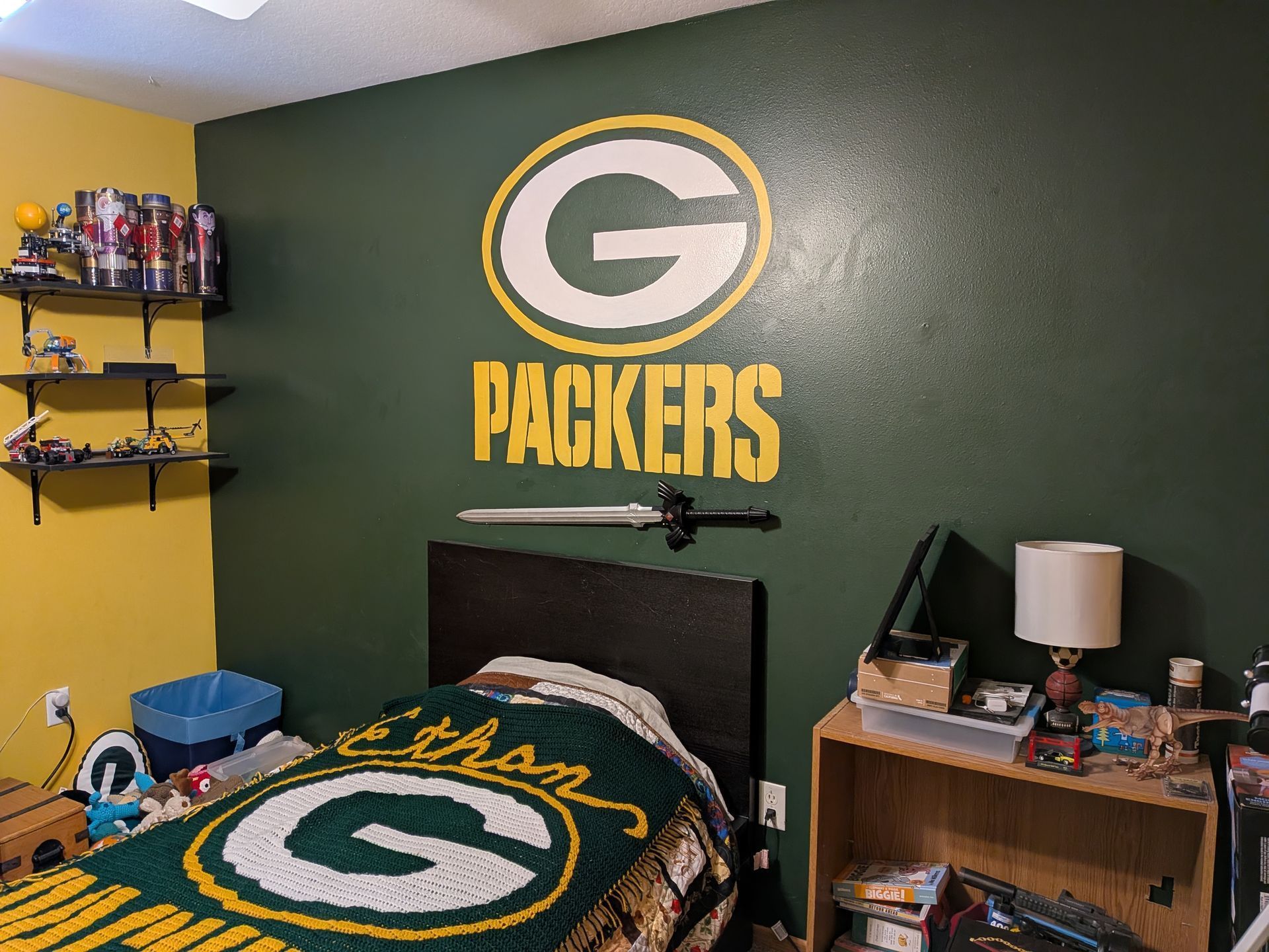 Green Green Bay Packers-themed bedroom with logo wall art, bed, and dresser under warm lighting
