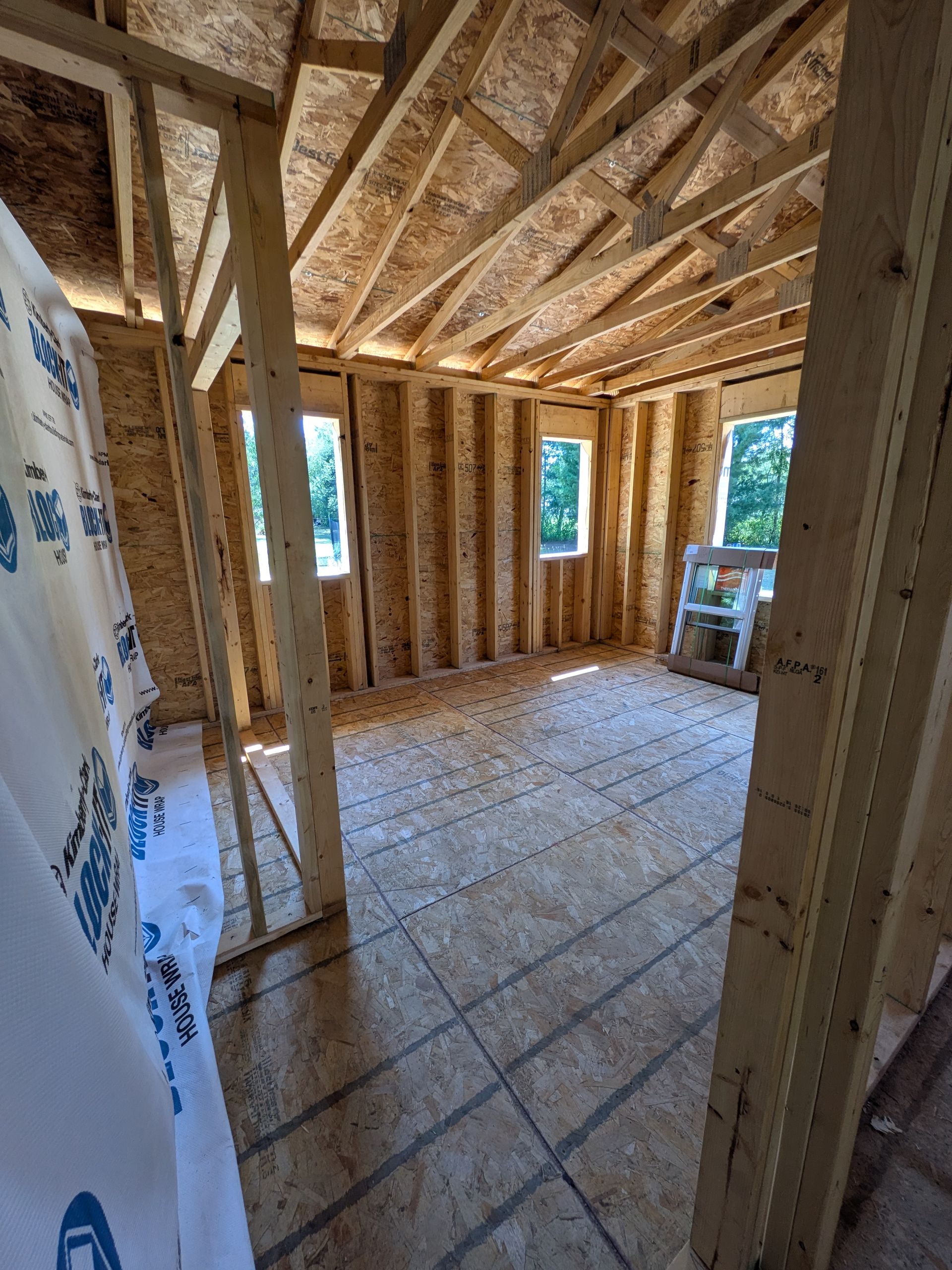 Interior of a house under construction with exposed wood framing, OSB floor, and open window and door openings.