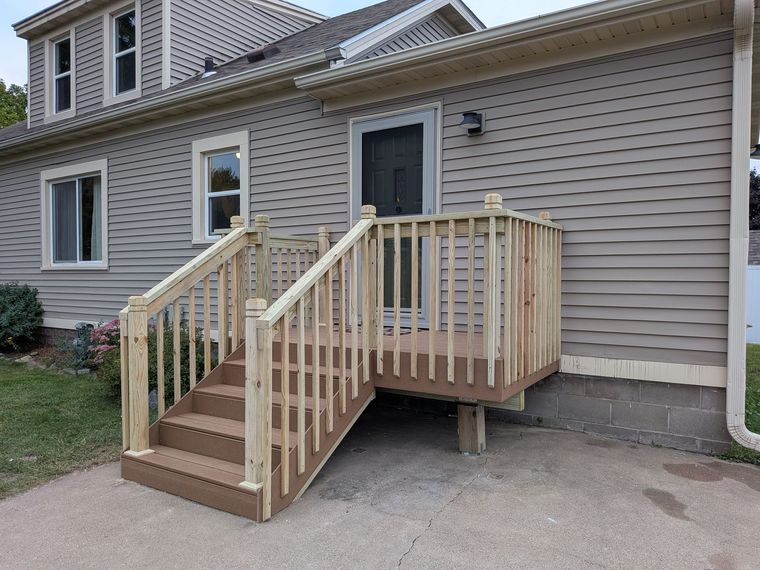 Wooden accessibility ramp and stairs leading to a side door of a beige house