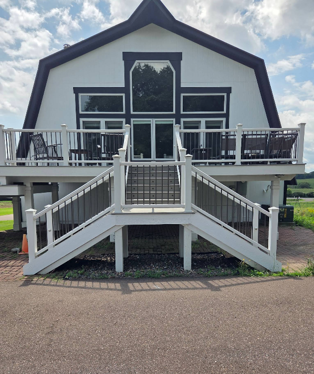 White barn-style building with a central staircase and wraparound deck on a cloudy day