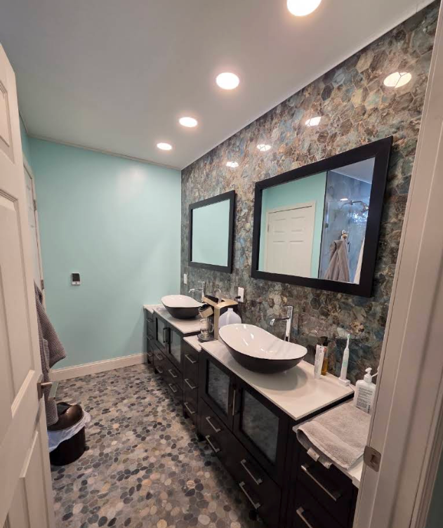 Modern bathroom with double sinks, black vanities, stone accent wall, and large mirrors